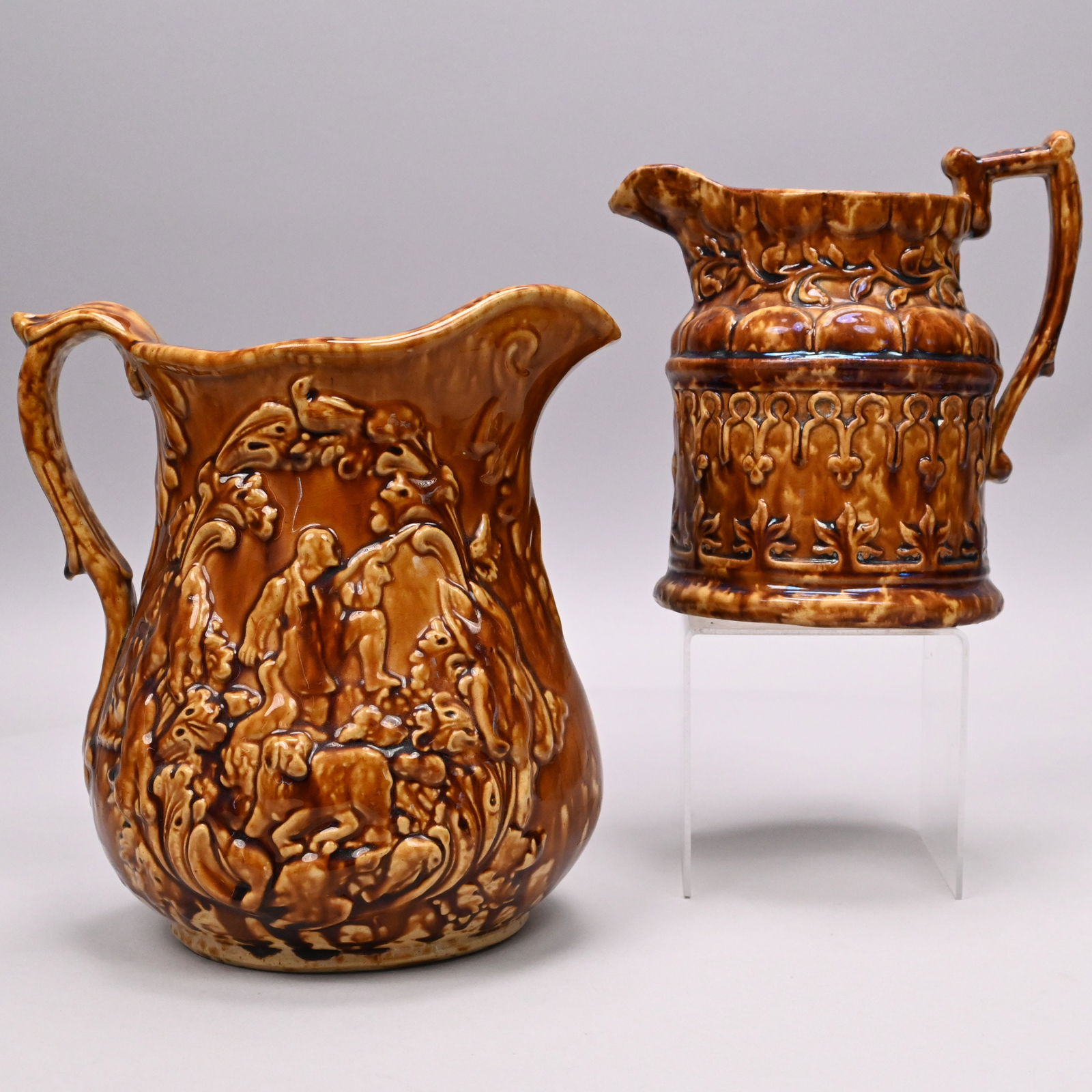 Two Rockingham-Glazed Yellow Ware Pitchers: Two Rockingham-Glazed Yellow Ware Pitchers, Second Half 19th Century. The first Gothic Revival and surrounded by borders of stylized leaves, horseshoe and trefoil arches, scalloped panels and vinery;
