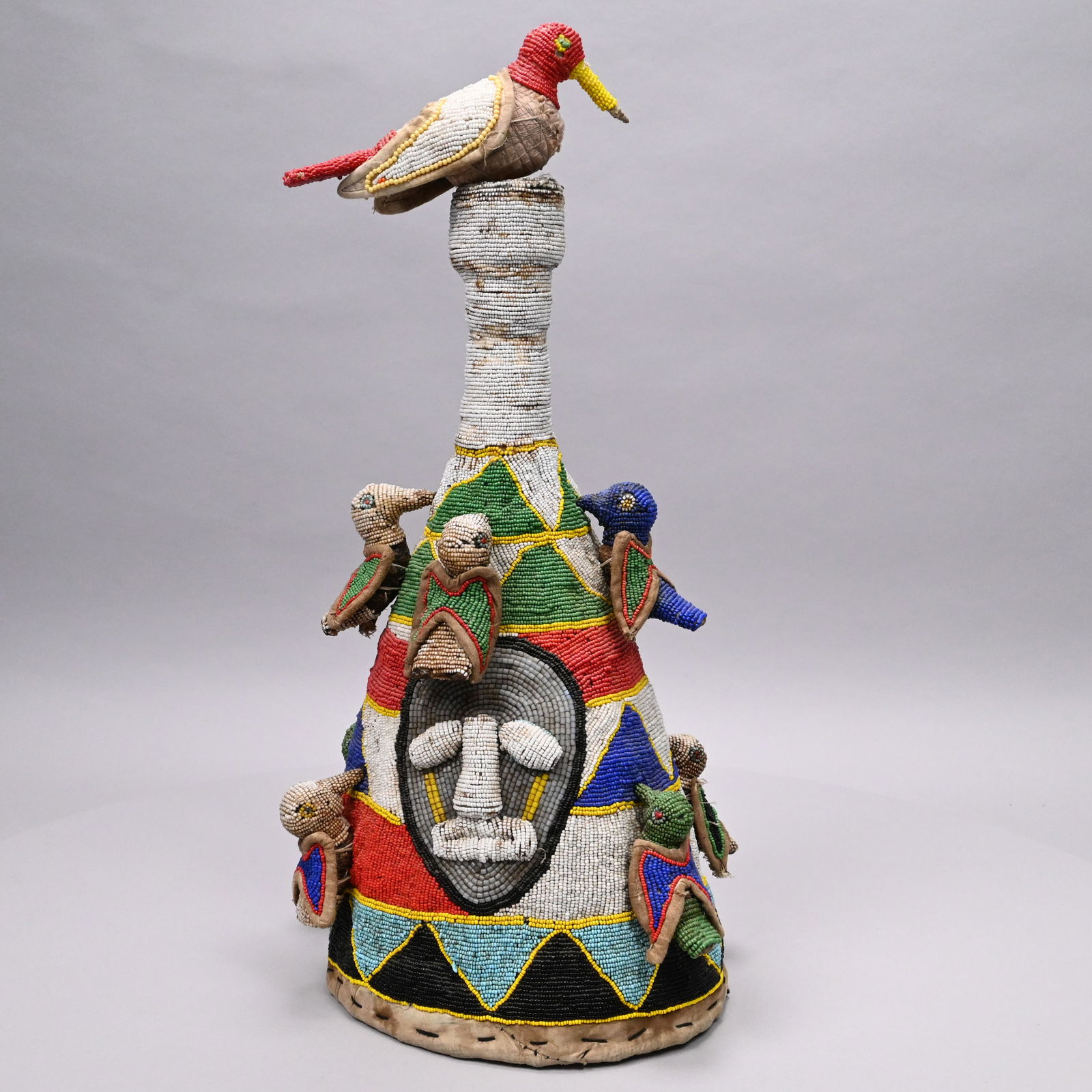 Yoruba Royal Beaded Headdress Crown (Ade), Nigeria: Yoruba Royal Beaded Headdress Crown (Ade), Nigeria, 20th Century. Of conical form, worked in rows of geometric patterns, stitched with a face mask and mounted with eight birds around the sides and one