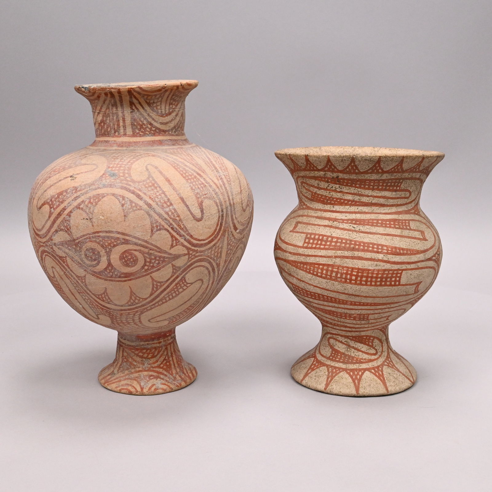 Two Ancient Thai Pottery Ban Chiang Burial Vessels: Two Ancient Thai Buff Pottery Ban Chiang Burial Vessels. Each painted in red on a cream-colored ground with abstract intricate repeating spiral, scroll, scalloped and wave designs.Smallest: H: 9.375