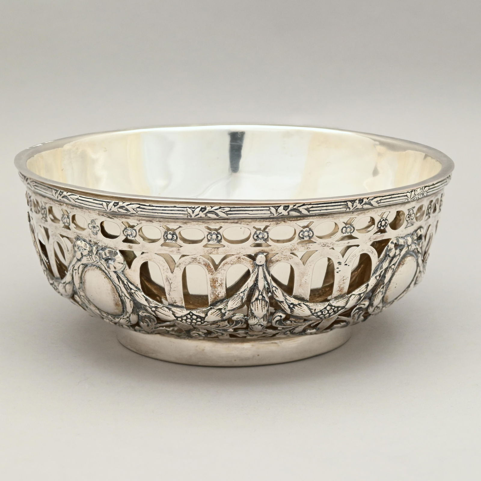 American Sterling Silver Serving Bowl with Liner: American Sterling Silver Serving Bowl, Twentieth Century. The pierced exterior sides surrounded by ribbon-tied oval wreaths joined by berried laurel leaf swags, above a border of berries and berried l