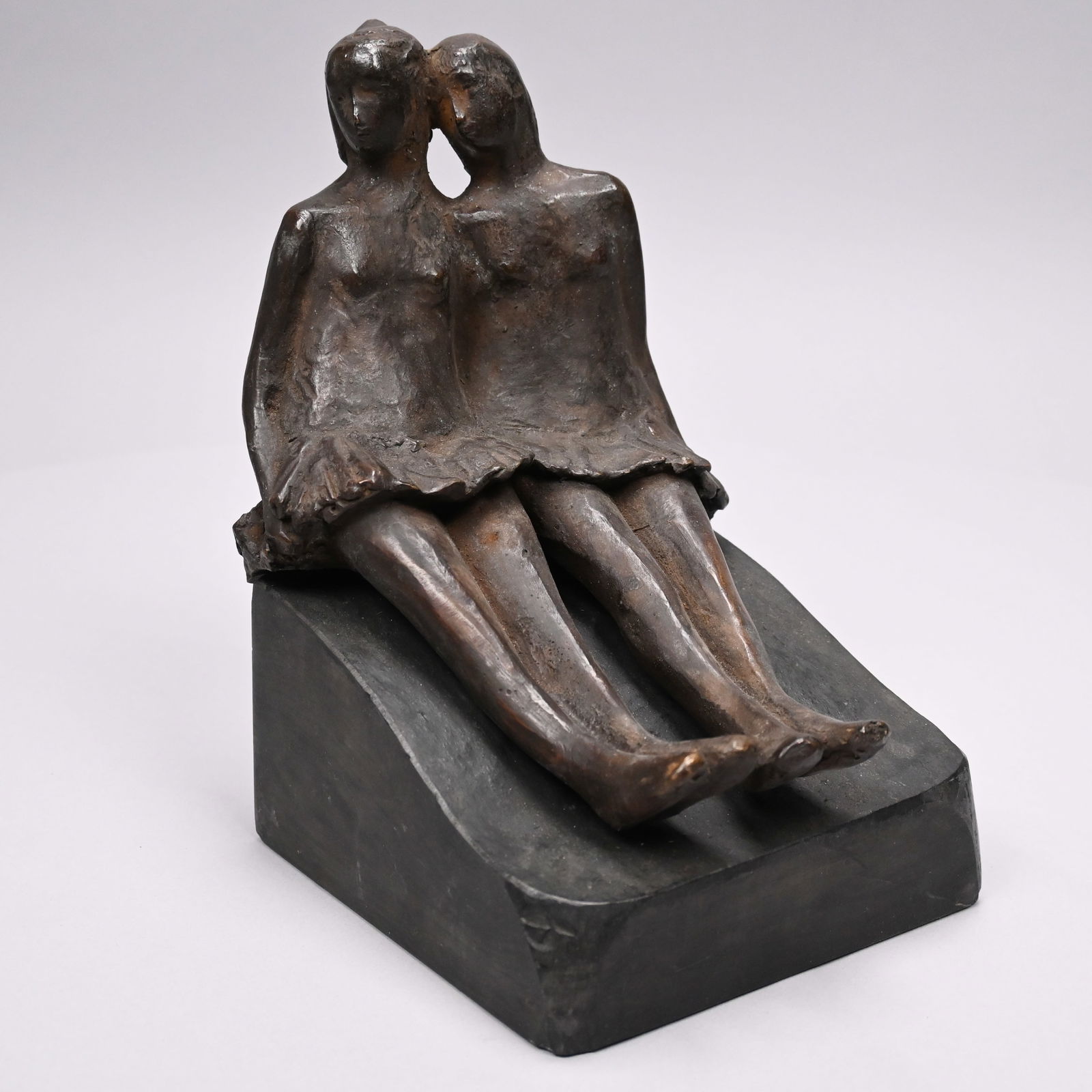 Patinated-Bronze Sculpture of Two Seated Dancers: Patinated-Bronze Sculpture of Two Seated Dancers. The brown-patinated figures of two young women cast as seated side-by-side on a sloping dark slate base, unsigned, no foundry mark.H: 9.5 in.