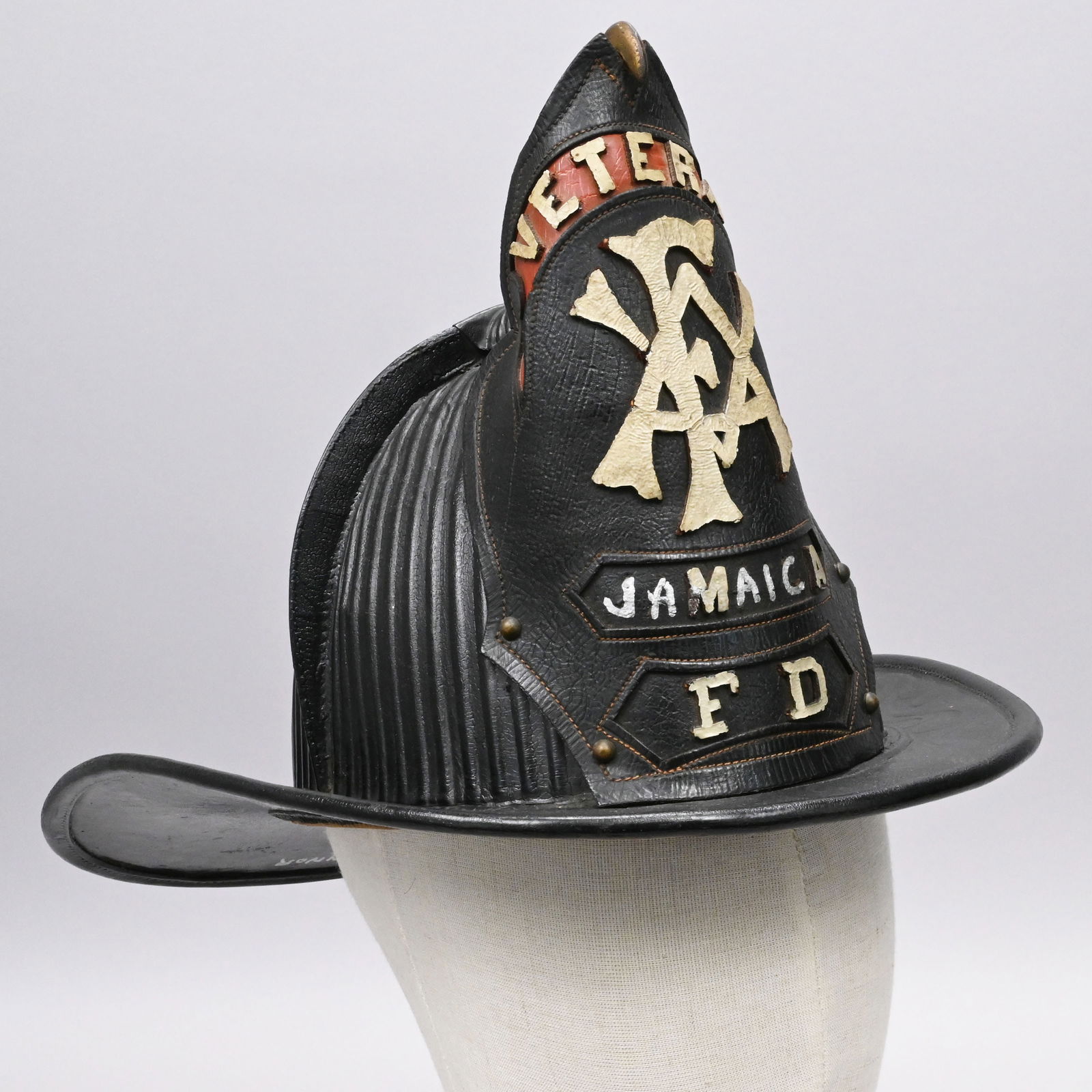 Veteran Jamaica Leather Fireman's Helmet: Veteran Jamaica Leather Fireman's Helmet, Circa 1906. The top of the helmet fitted with four combs and a gilt eagle front piece holding the shield "VETERAN" in white letters on a red ground, above