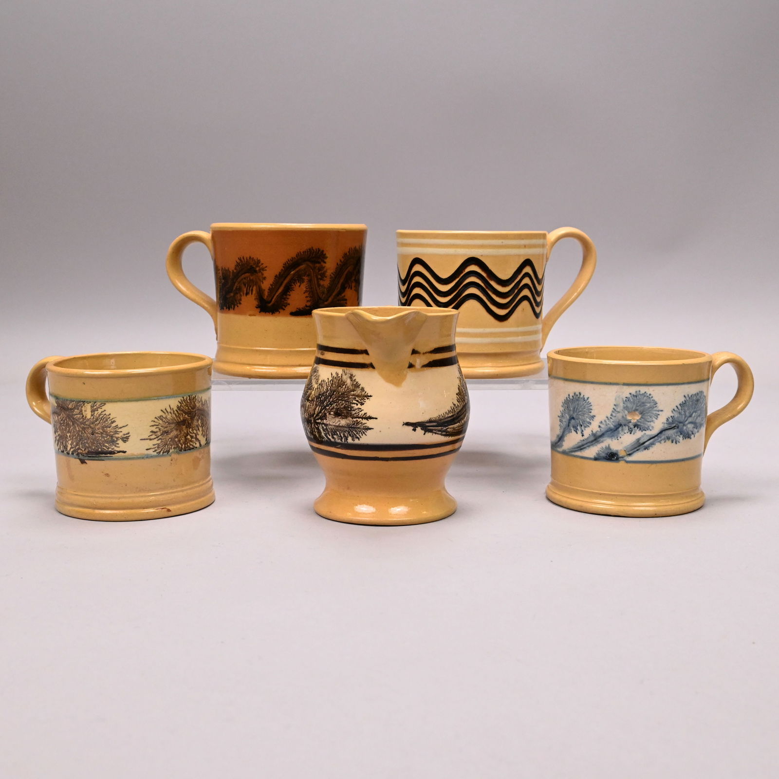 Four Yellowware Slip-Banded Mochaware Mugs&Pitcher: Four Yellowware Slip-Banded Mochaware Mugs and a Milk Pitcher, British or American, 1840-1870. Slip-banded in dark brown, blue or white, surrounded by blue or brown dendritic leaves and stems or