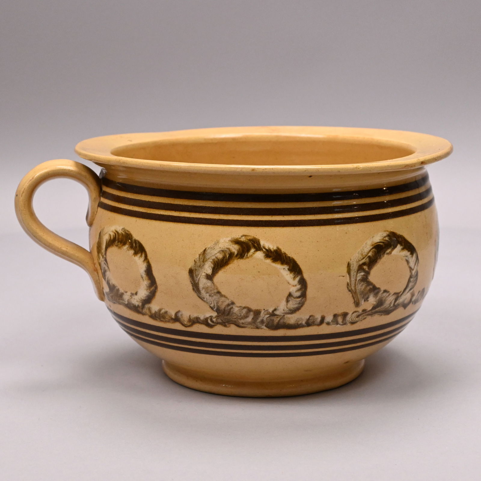 Yellowware Slip-Banded Mochaware Chamber Pot: Yellowware Earthworm Slip-Banded Mochaware Chamber pot, 1840-1870. Slip-banded in dark brown and centering a slip-trailed white and brown looping earthworm.H: 5 in., W: 9.25 in., Diam: 8.25 in.