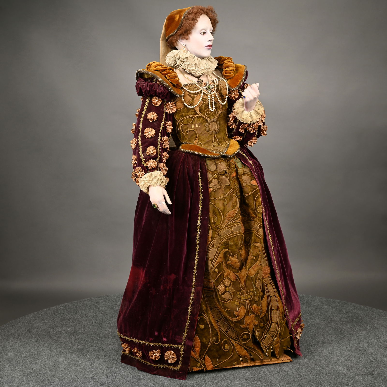 Elaborate Elizabethan Woman's Costume: Elaborate Elizabethan Woman's Costume. The life-sized mannequin dressed in a gown constructed of rich plum and tawny-colored velvets with trapunto embroidered bodice and underskirt, lace cuffs and