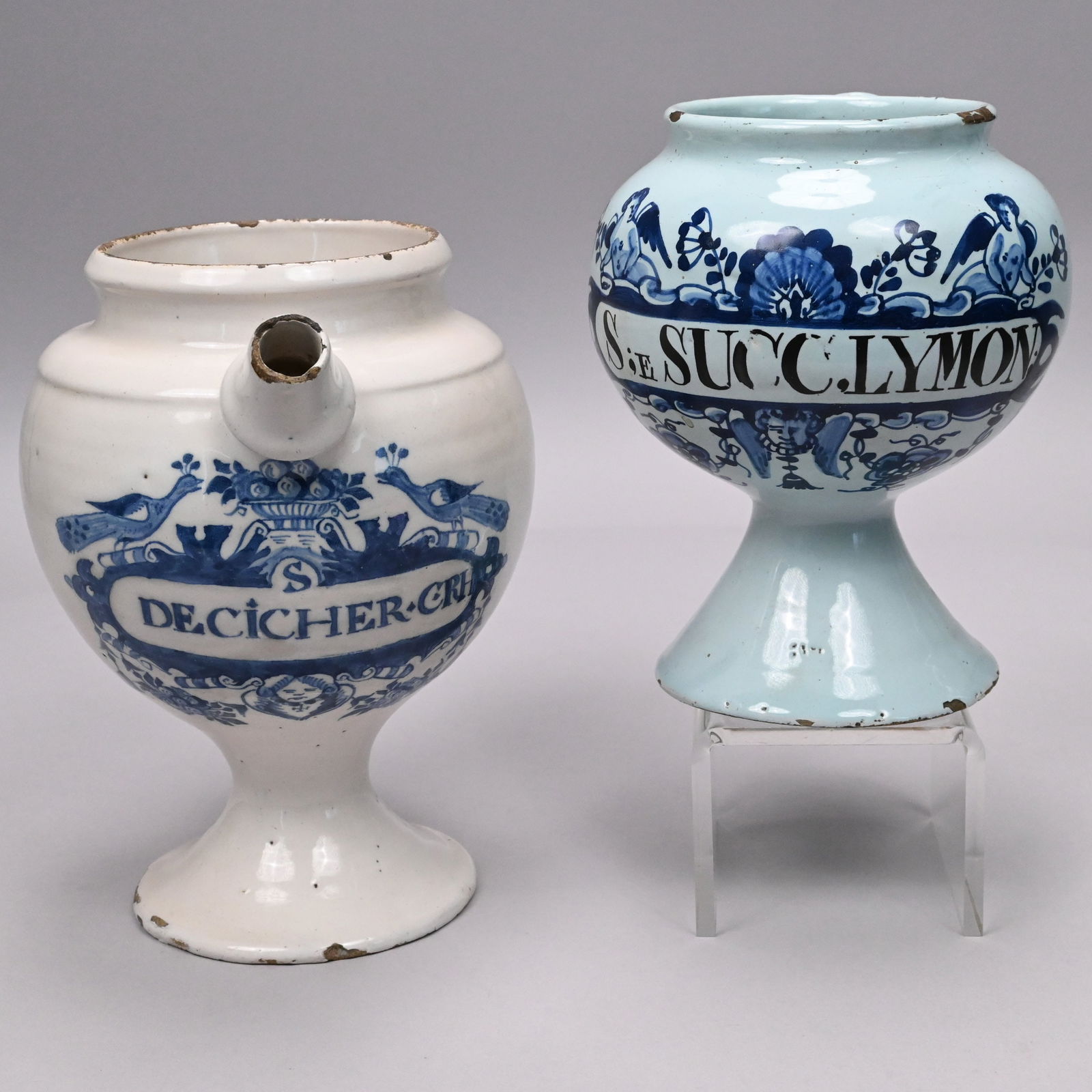 Two Delft Blue and White Wet Drug Jars: English Delft Blue and White Wet Drug Jar and a Dutch Delft Example, 18th Century. The first painted with a label inscribed "S;E SUCCLYMON," surmounted by a pair of putti centering a shell, above a