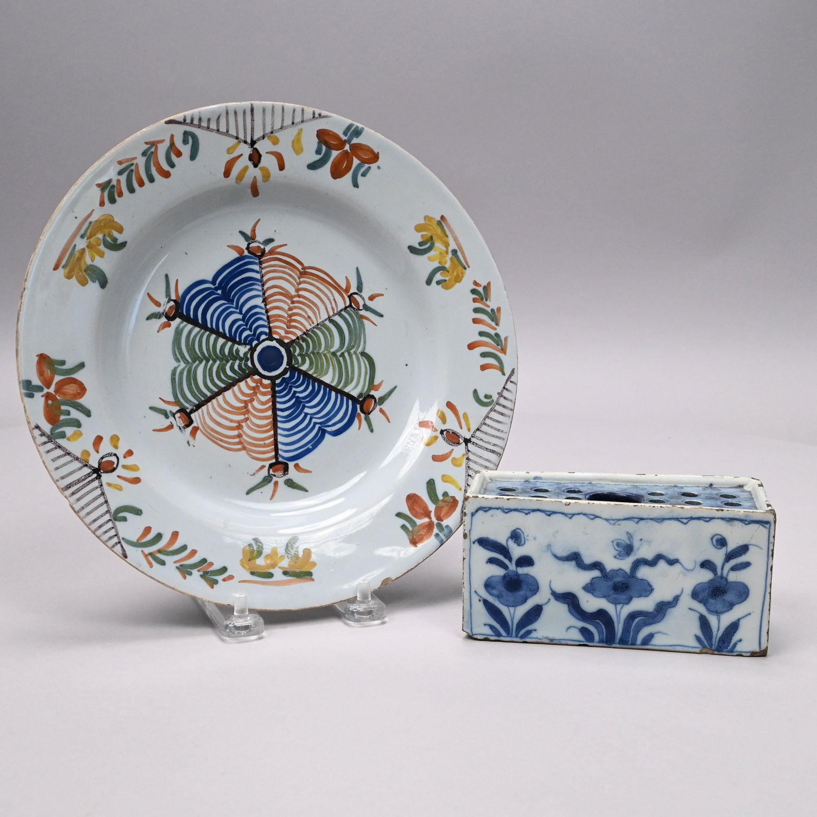 English Delft Flower Brick and a Plate: English Delft Blue and White Flower Brick, Lambeth, Circa 1740-1750; and a Polychrome 'Spiderweb' Plate, 1780-1800. The flower brick rectangular with one large opening within eighteen smaller holes,