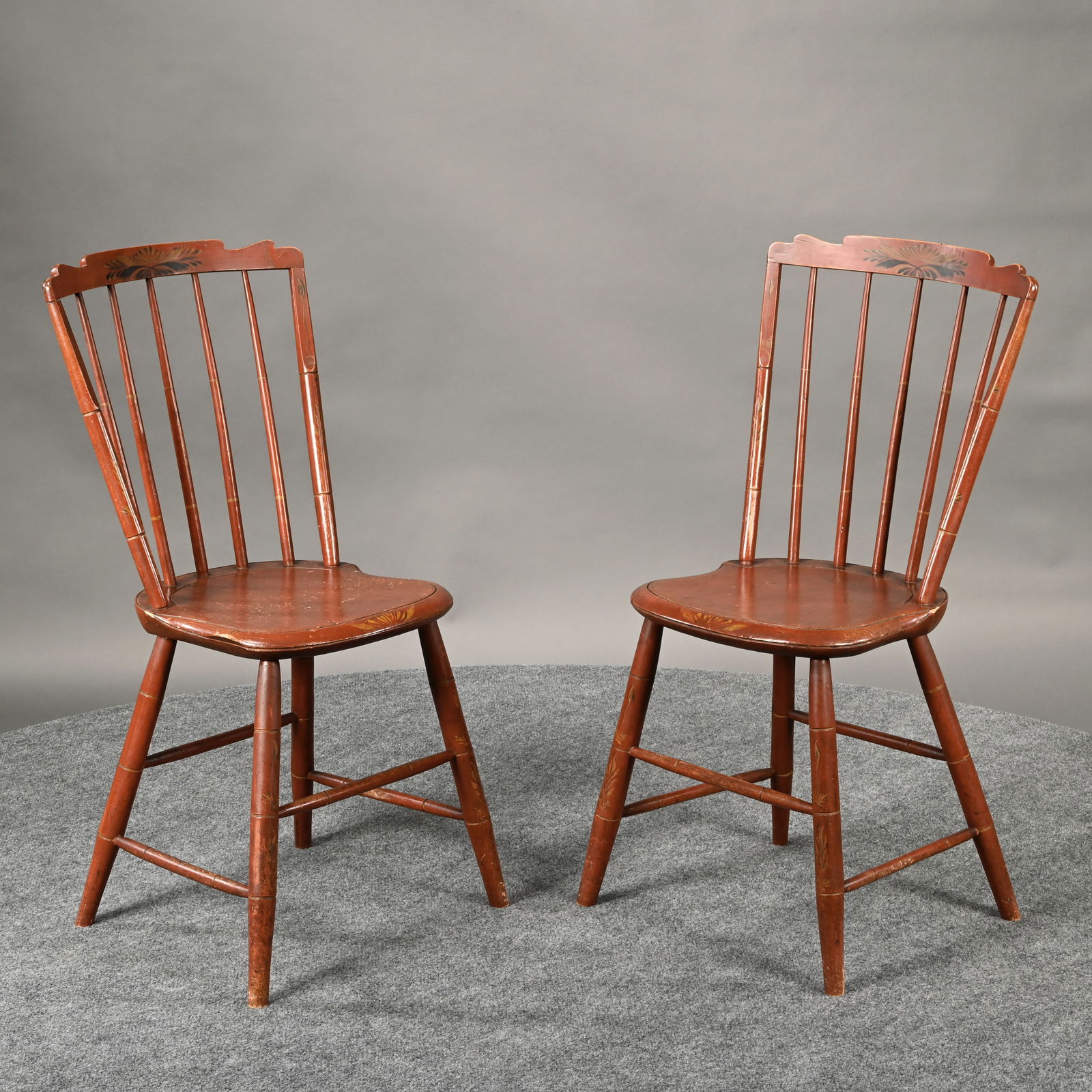 Pair New England Painted Step-Down Windsor Chairs: Pair of New England Red Painted Step-Down Windsor Chairs. Each with paint decorated scalloped crest rail above a five-spindle back, over a shaped plank seat, raised on splayed, bamboo-turned legs.H: