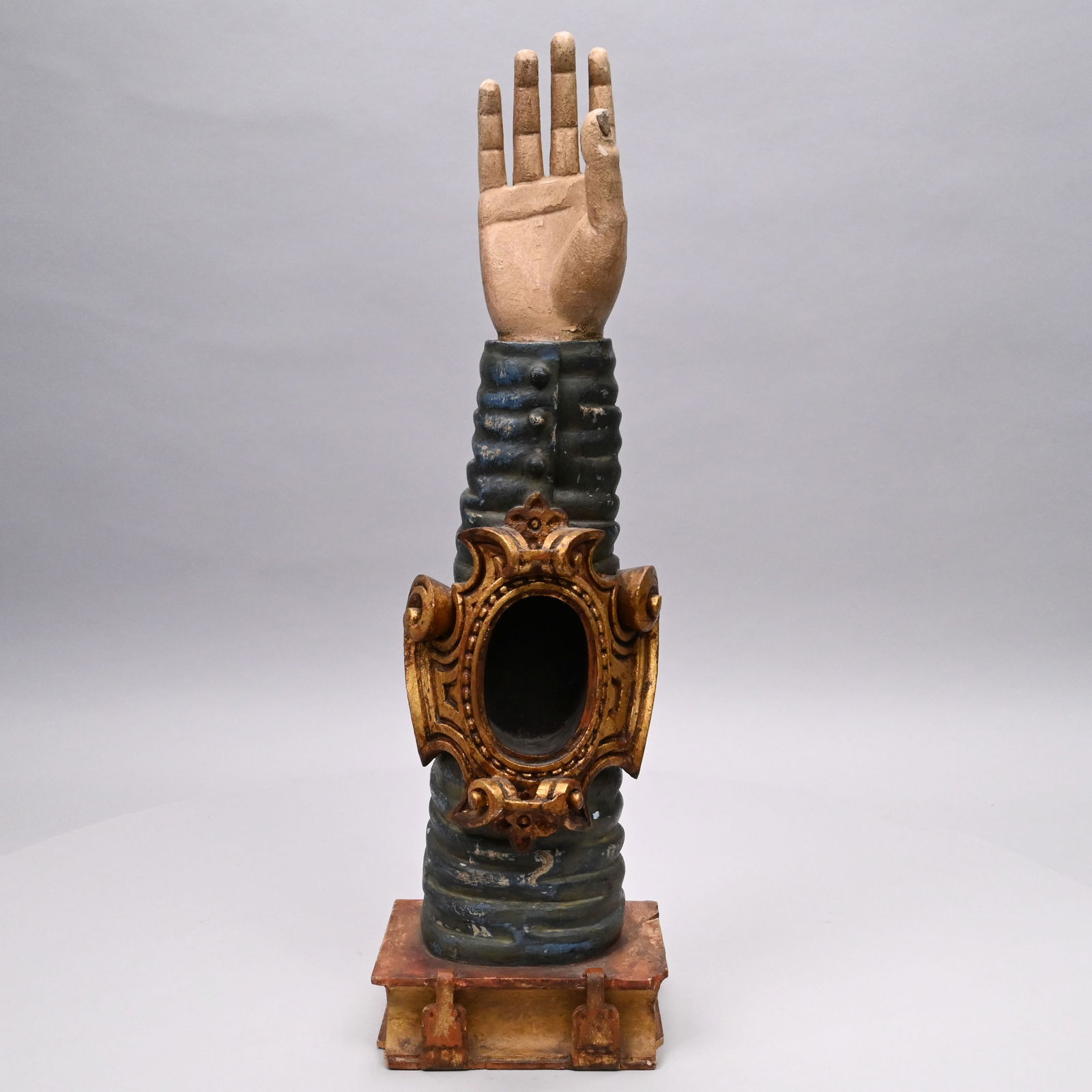 Continental Carved and Painted Reliquary Arm: Continental Carved and Painted Reliquary Arm. The blue sleeve carved with a gilt cartouche with oval opening, set on a bible with clasps.H: 22.5 in., W: 6.375 in., D: 5.5 in.