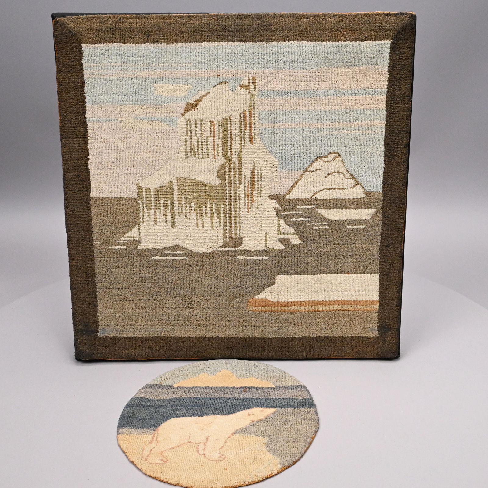 Pictorial Hooked Mat and a Table Mat, Grenfell: Pictorial Wool and Silk Hooked Mat and a Table Mat, Grenfell Labrador Industries, Newfoundland, 1930s. The first worked in blue, brown and ivory yarns with a view of icebergs; the second in blue,