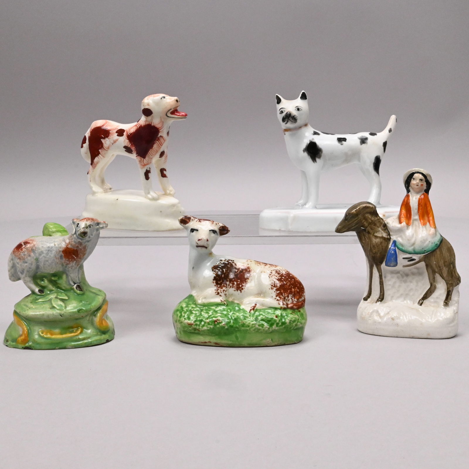 Four Staffordshire Animals and a Figural Group: Four Staffordshire Animals and a Figural Group, 1810-1860. Comprising a pearlware figure of a lamb sponged with brown spots, a pottery figure of a recumbent cow sponged with brown spots, a