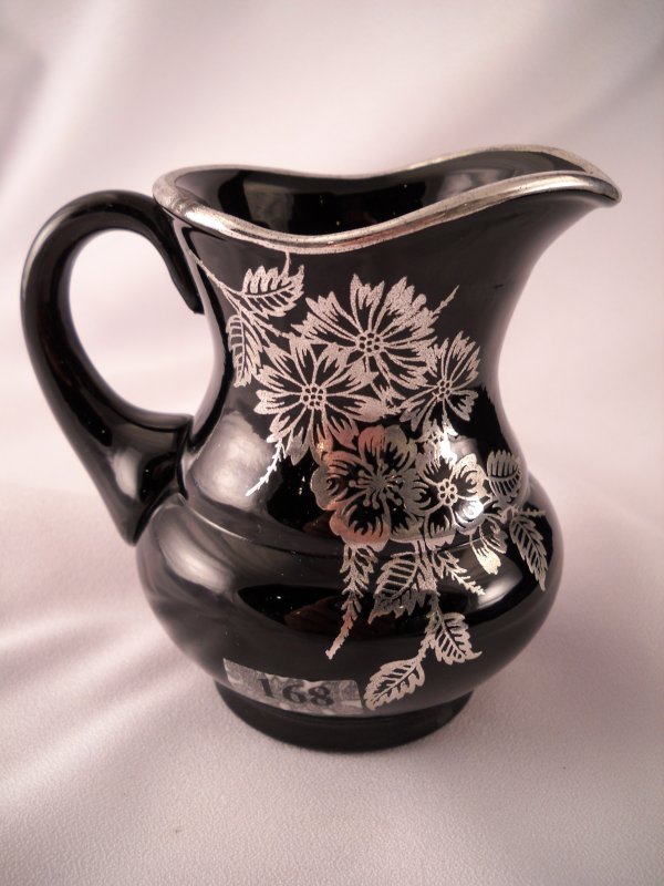Experimental decoration: This black 4.5" tall crea: Experimental decoration: This black 4.5" tall creamer with applied black handle has been decorated with a silver overlay floral and leaf motif, and it also has a silver top edge. Made ca. 1980.