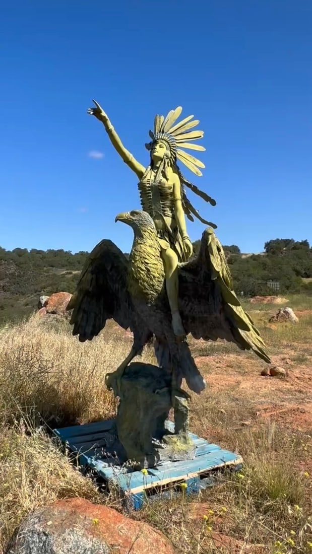 Monumental Indian Woman Riding American Eagle Bronze Sculpture: Measurements : 108” H x 90” L Intricate outdoor sculpture is made of a durable material with a yellow-green finish. This piece depicts a woman wearing a large feathered headdress and a