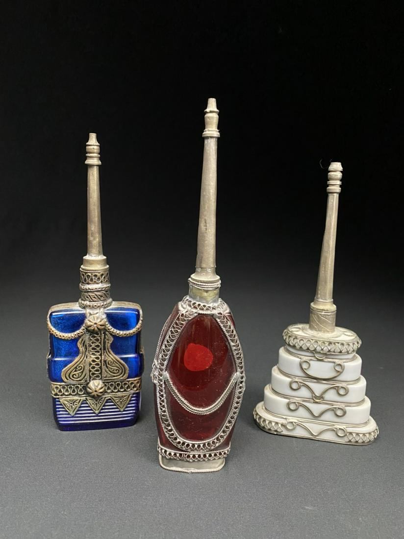 A Collection of Islamic rose water Bottles: Three vintage Middle Eastern rose Water perfume sprinkler vessels with metal ornamentation, one base-inscribed in French.