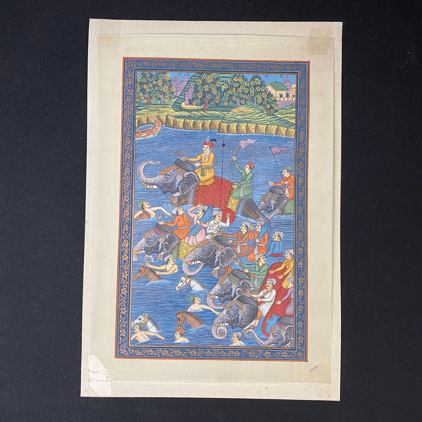 Mughal Style Painting on Silk Crossing the River: Mughal style painting on silk depicting a group of men crossing a river. The artwork is tapped on a board that has writing on the back.
