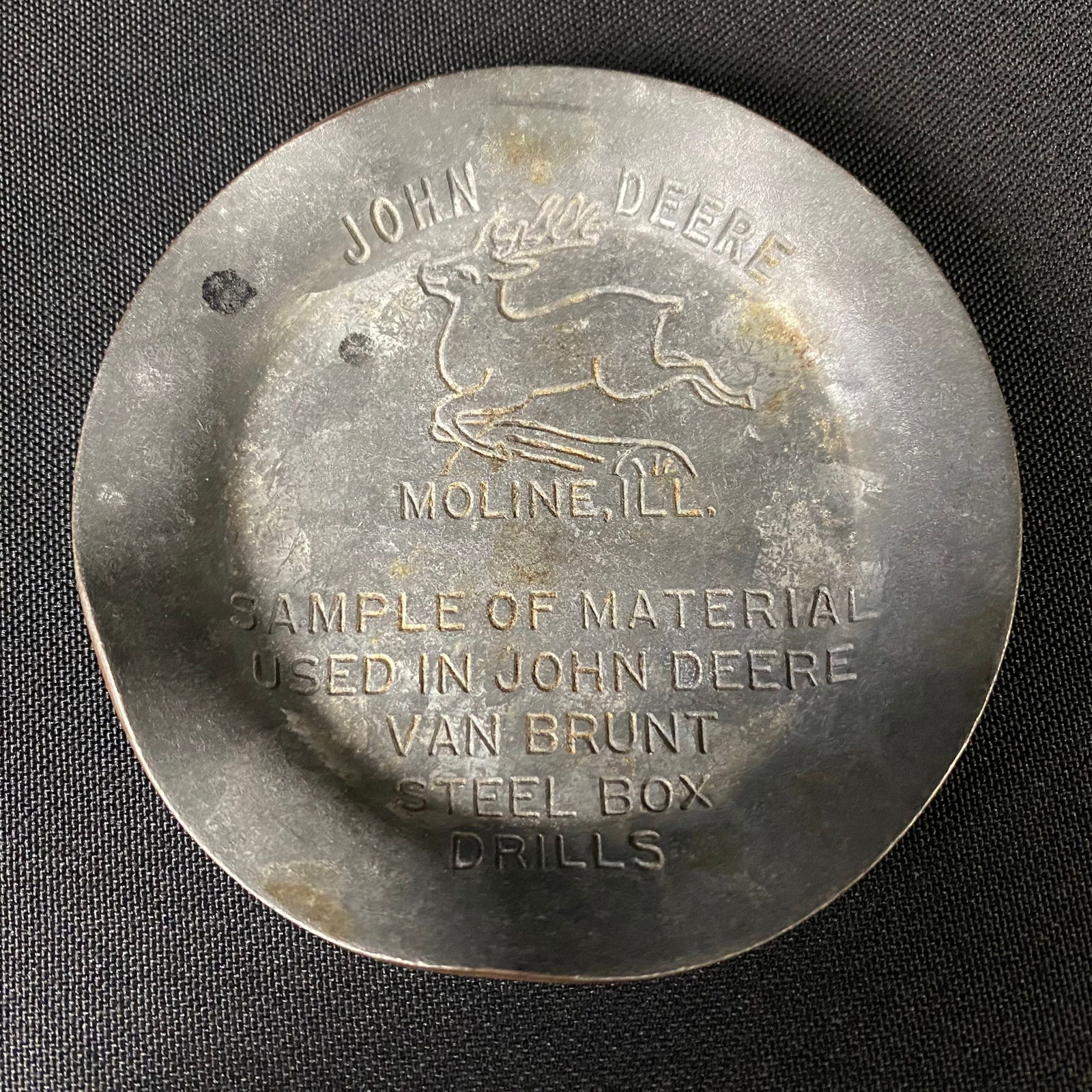 John Deer Steel Ashtray: John Deere Steel Ashtray. Condition is great with the stamped details maintain crisp lines. It has a light natural patina, and has been bent a in a few spots along the brim, as it was a sample piece t