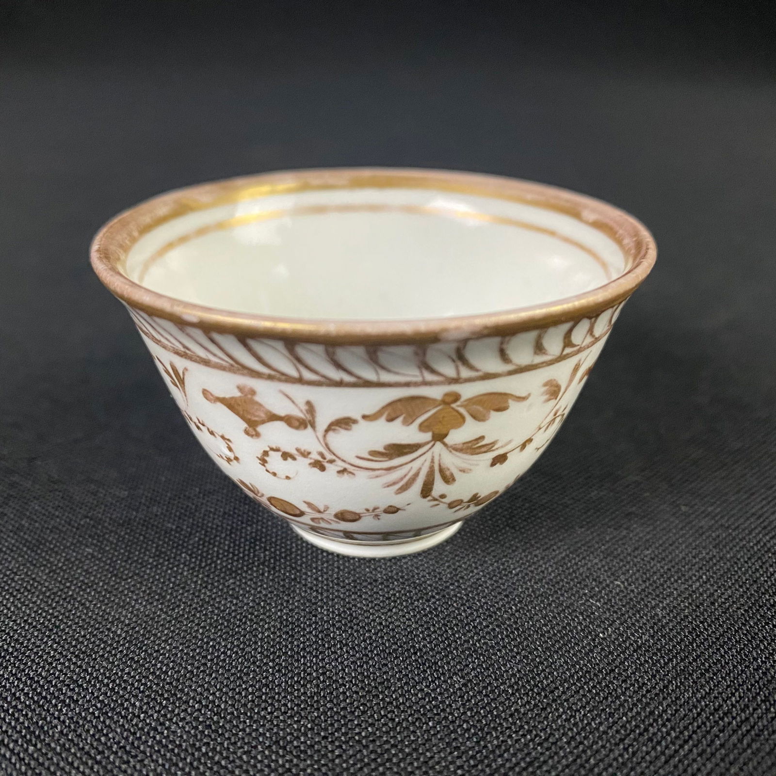 Small Gold and White Tea Cup: Small Gold and White Tea Cup. It is in great condition with some surface wear, causing the gold glaze details to have faded in some spots, as well as some miniscule chipping along the inside edge of t