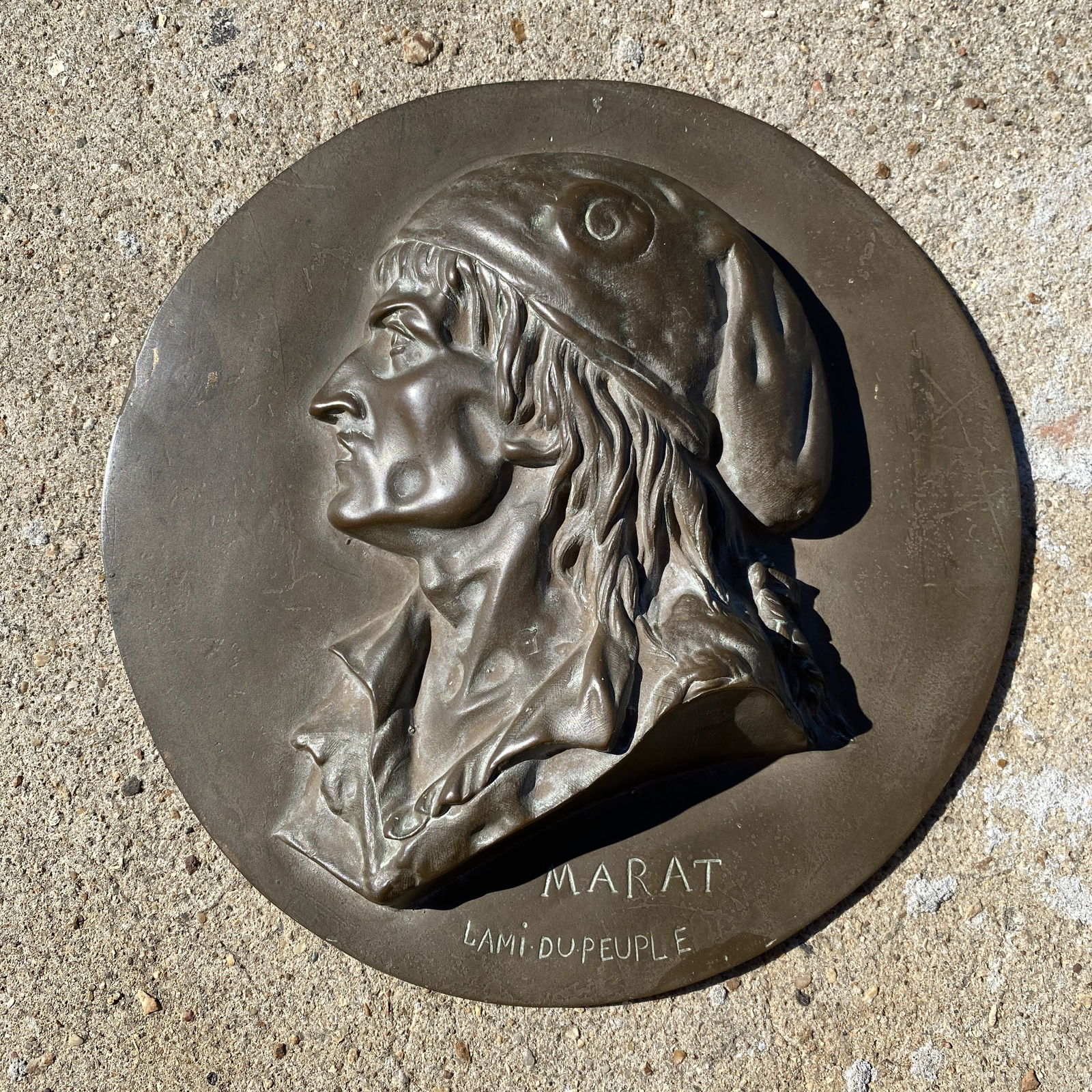 Antique Plaque of Marat Du Peuple: Antique Plaque of Marat Du Peuple. The piece of made of a cast material that has some traces of gilding. The surface appears similar to bronze. The diameter is 8.2".