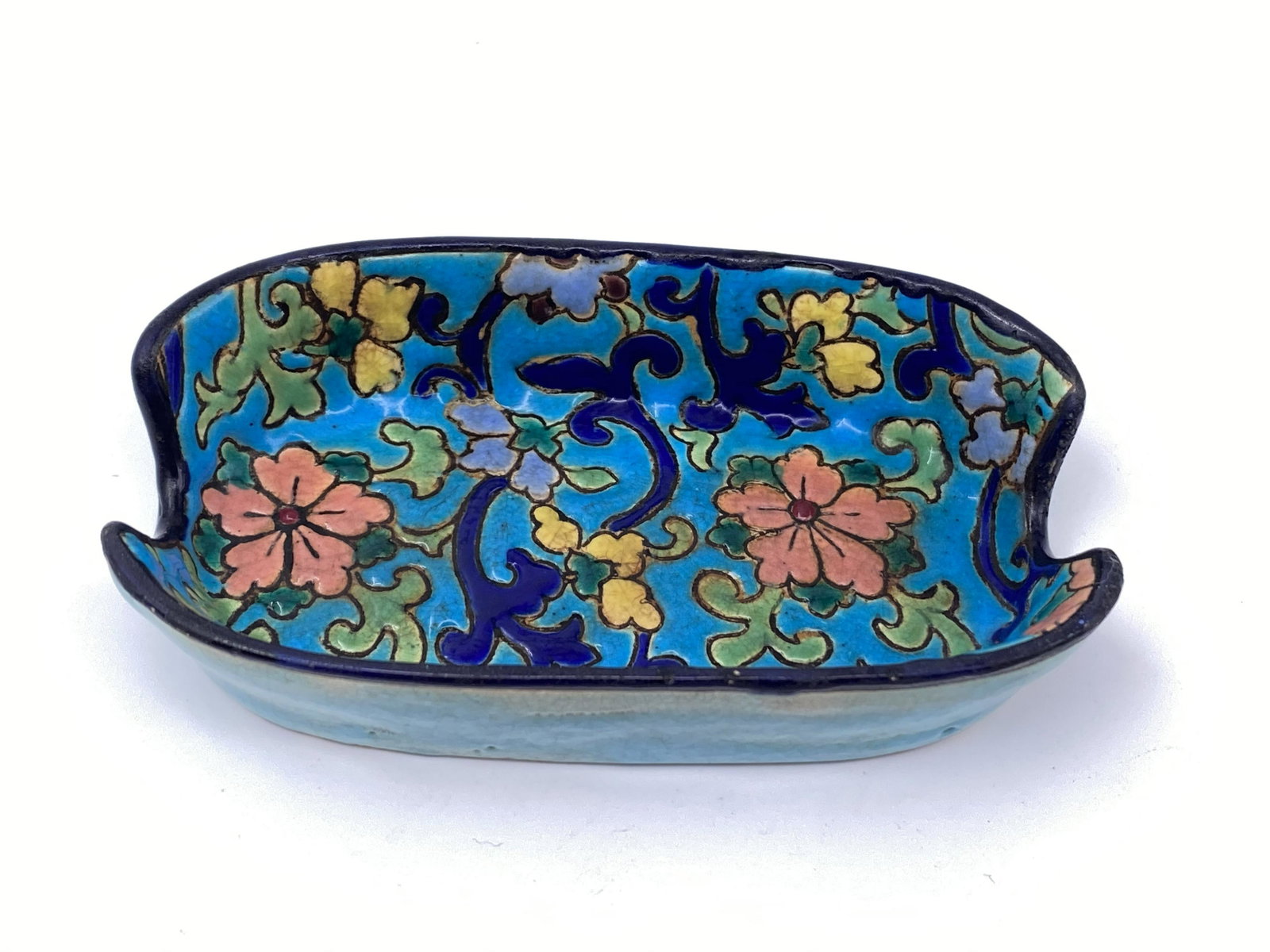 Longwy turquoise floral motif ashtray: This sweet little ashtray is in a hand painted enamel highly textured majolica. A bright turquoise blue base is decorated with multi-colored various flowers traditional for Longwy design. The bottom r