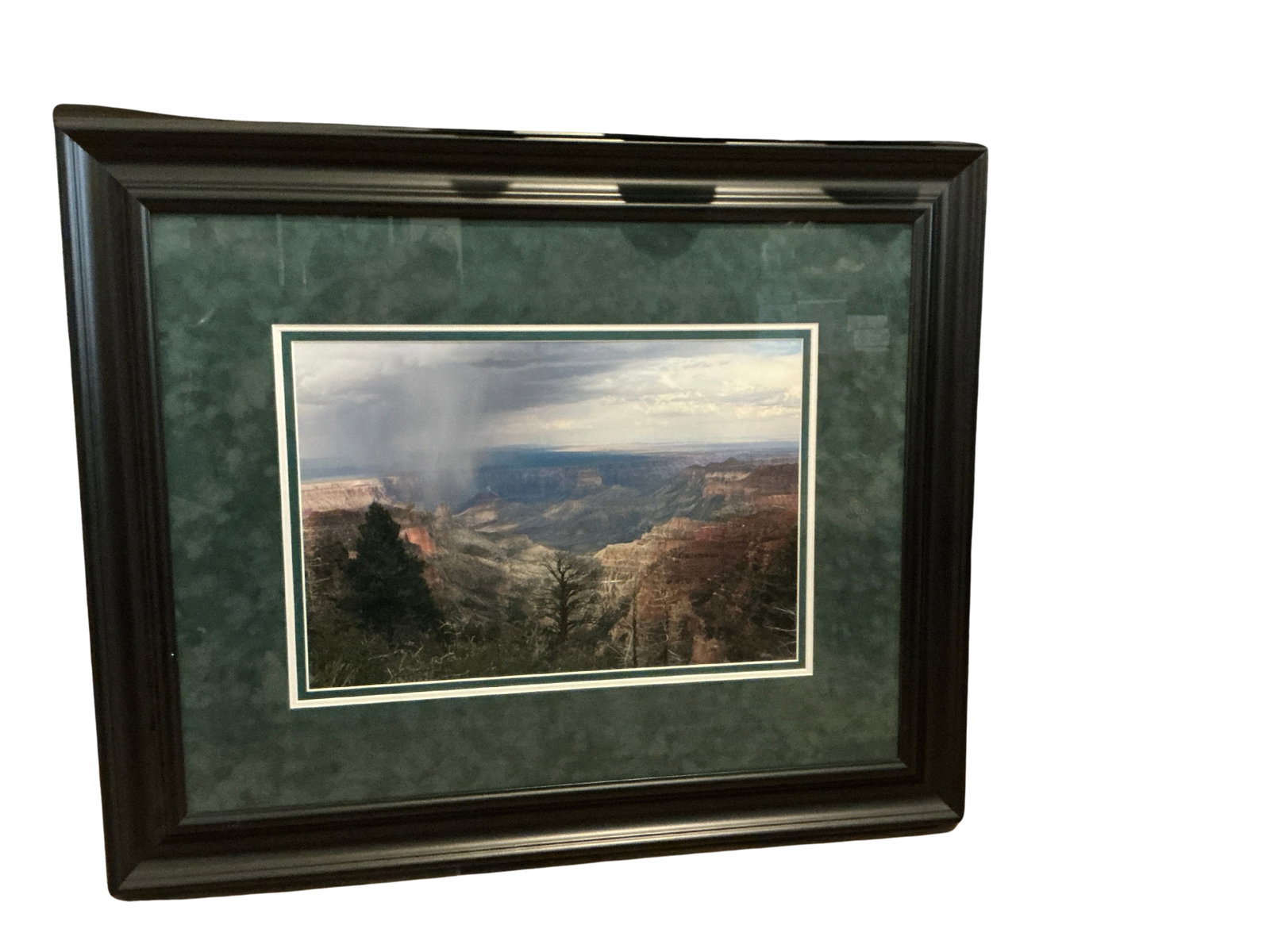 Framed Landscape Photograph with Green Mat: This is a framed photograph depicting a striking landscape view, possibly of a natural canyon with dramatic cloud formations suggesting an impending storm. The artwork is encased in a dark wooden fram
