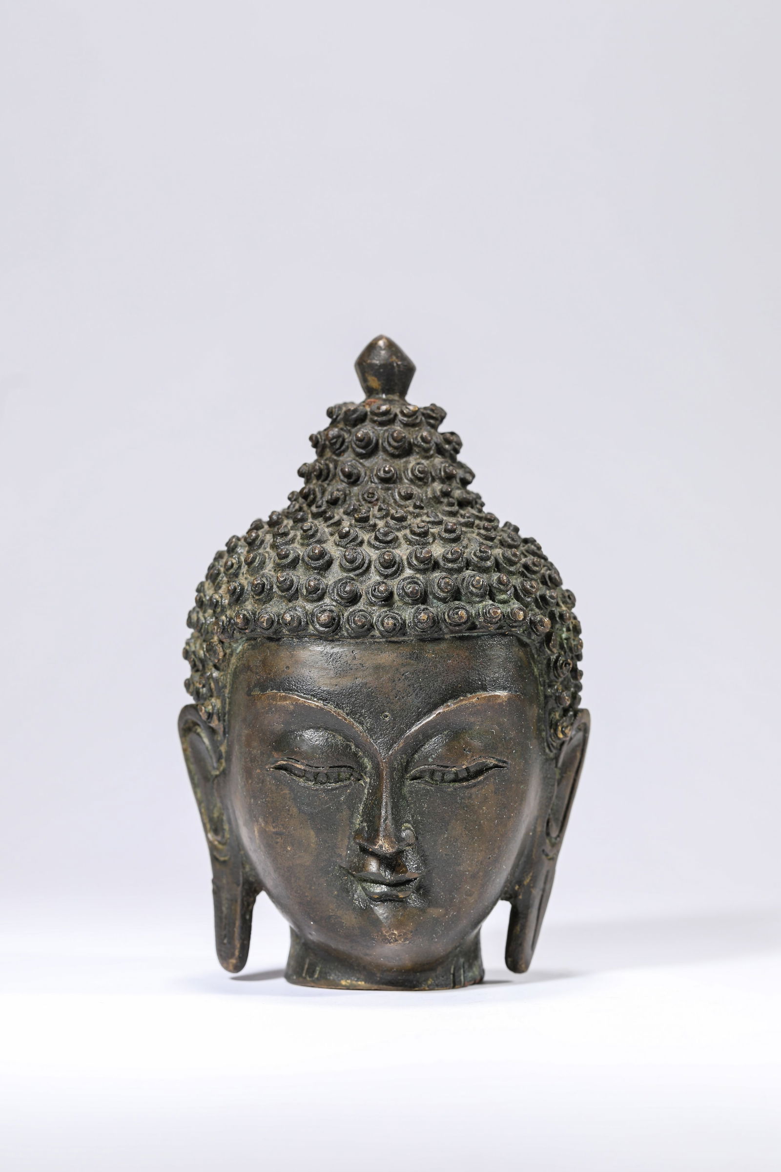A BRONZE HEAD OF BUDDHA: A BRONZE HEAD OF BUDDHA Dimensions: Weight: 543g. Length: 8.5 cm (3.35 in) x Width: 8.0 cm (3.15 in) x Height: 13.5 cm (5.31 in). All measurements are approximate.