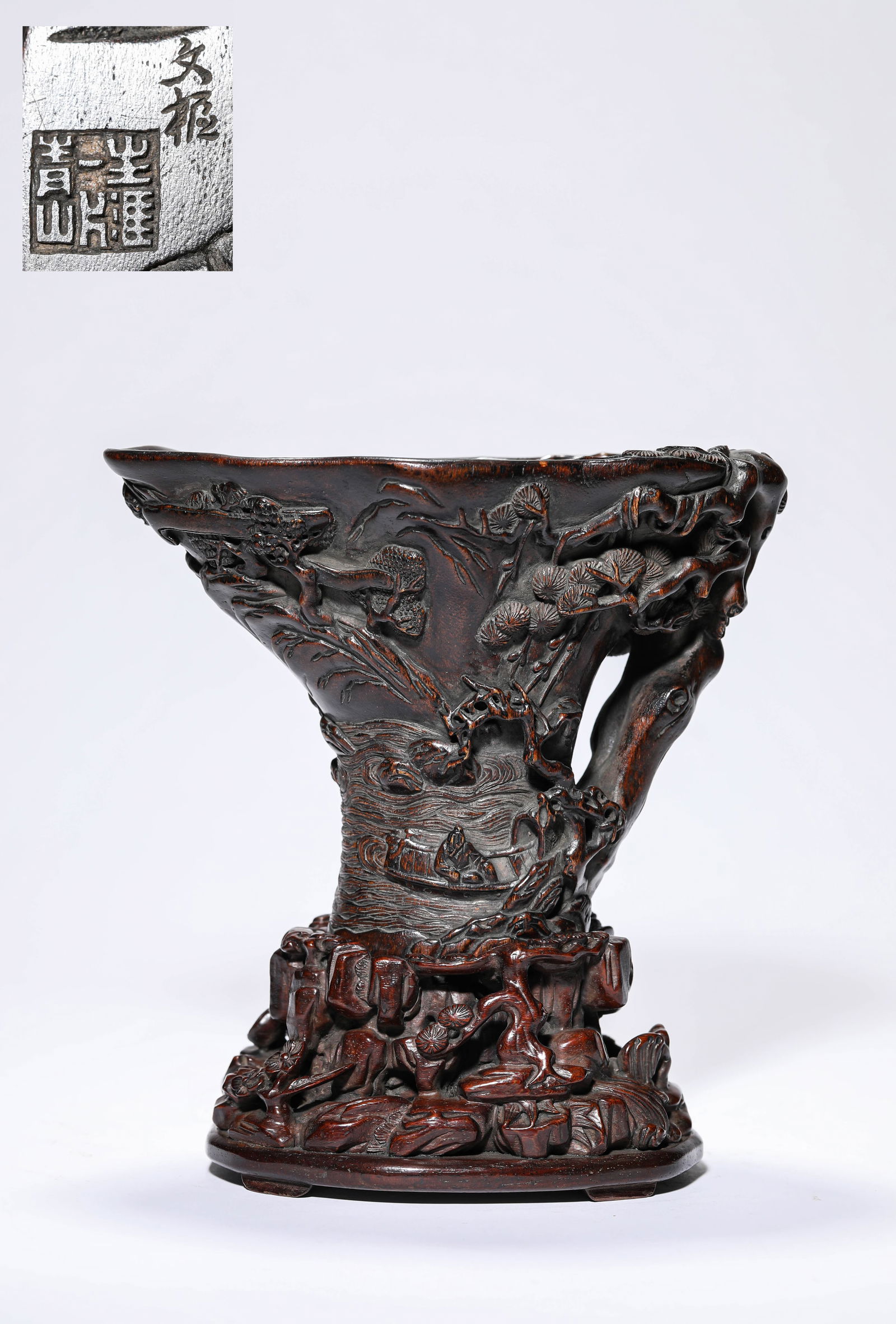 A WOOD 'CARVED SCHOLARS UNDER A PINE TREE' 'RHINOCEROS HORN-FORM' CUP: A WOOD 'CARVED SCHOLARS UNDER A PINE TREE' 'RHINOCEROS HORN-FORM' CUP Dimensions: Length: 17.4 cm (6.85 in) x Width: 11.0 cm (4.33 in) x Height: 12.5 cm (4.92 in). All measurements are approximate.