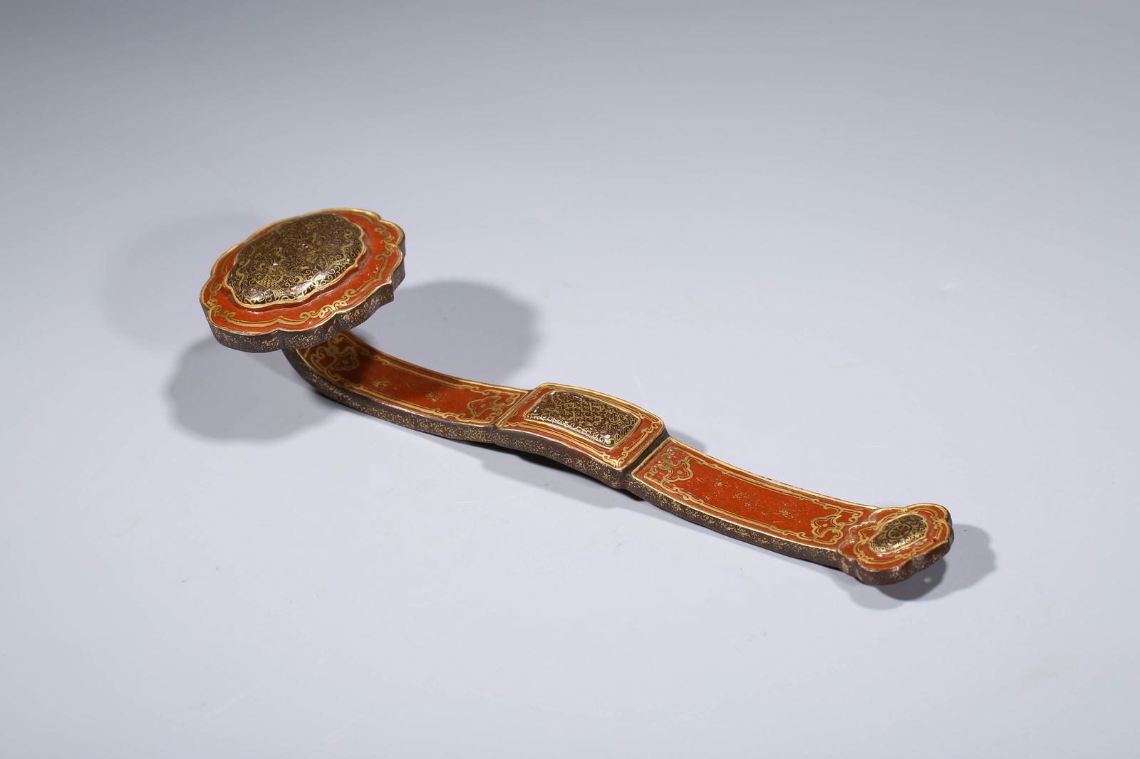 A CORAL-RED-GROUND GILT-DECORATED RUYI SCEPTRE: A CORAL-RED-GROUND GILT-DECORATED RUYI SCEPTRE Dimensions: Length: 8.2 cm (3.23 in) x Width: 27.2 cm (10.71 in) x Height: 5.4 cm (2.13 in). All measurements are approximate.