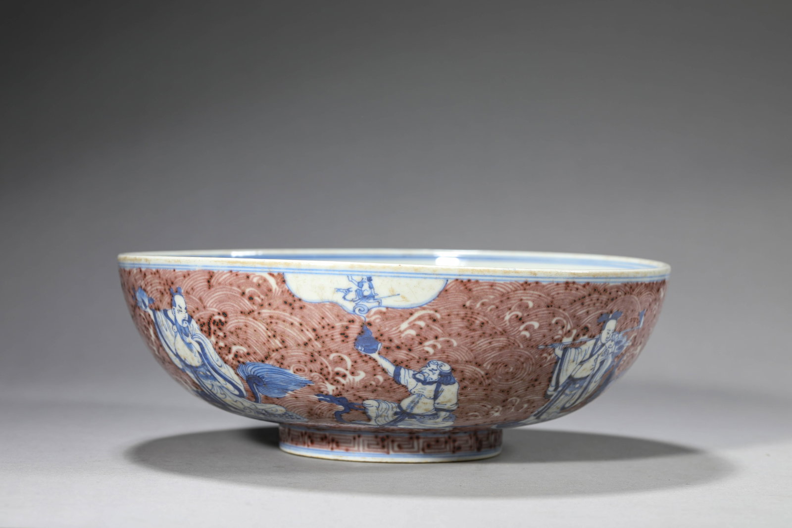 A BLUE AND WHITE AND UNDERGLAZE-RED 'EIGHT IMMORTALS OFFERING SHOU' BOWL: A BLUE AND WHITE AND UNDERGLAZE-RED 'EIGHT IMMORTALS OFFERING SHOU' BOWL Dimensions: Width: 23.2 cm (9.13 in) x Height: 8.1 cm (3.19 in). All measurements are approximate.