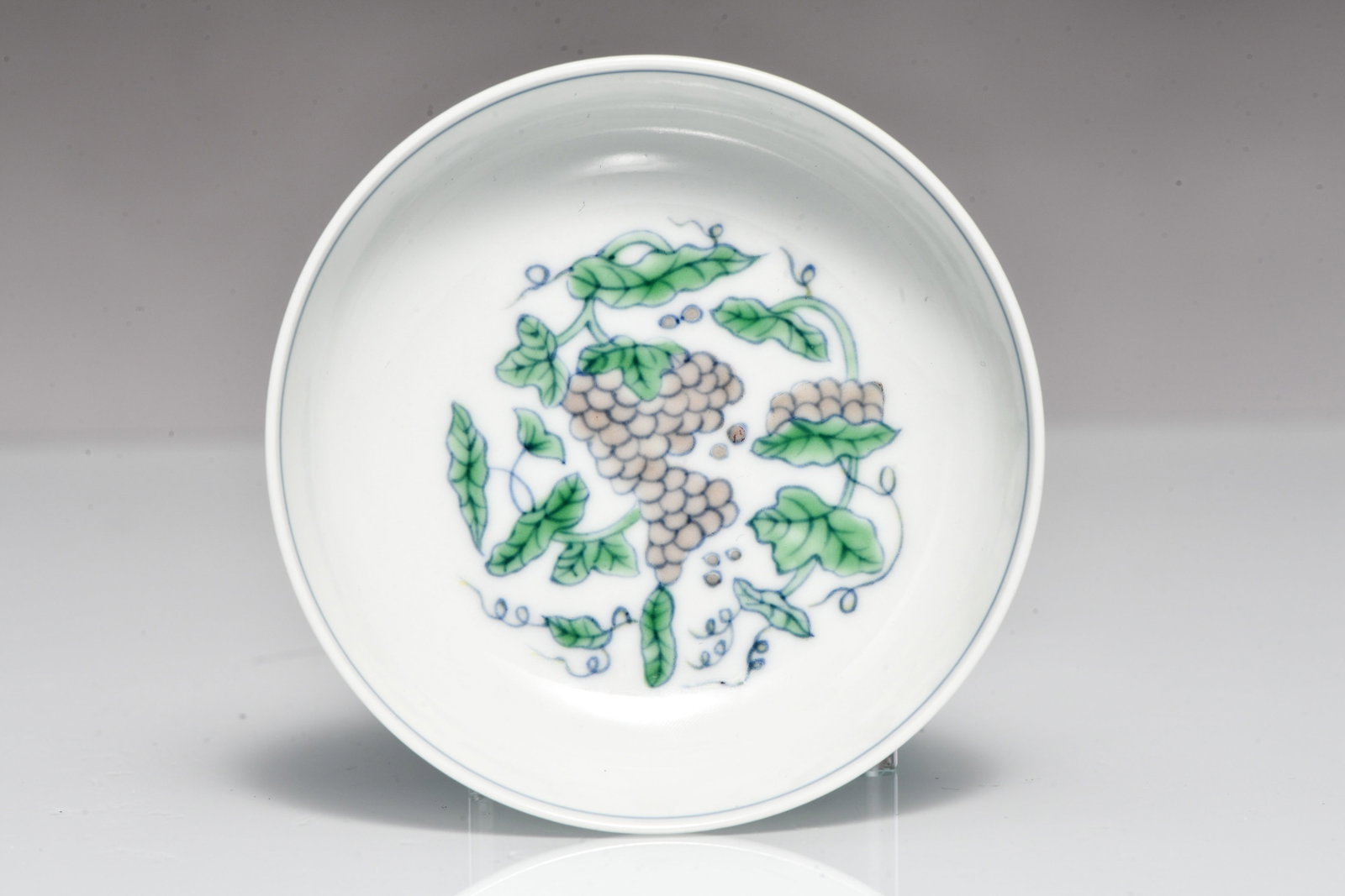 CELADON-GLAZED SMALL PLATE WITH LOTUS-LEAF PATTERN AND GRAPE DESIGN, MADE DURING THE REIGN OF: CELADON-GLAZED SMALL PLATE WITH LOTUS-LEAF PATTERN AND GRAPE DESIGN, MADE DURING THE REIGN OF EMPEROR CHENGHUA OF THE MING DYNASTY Description: Width: 8.2 cm Height: 2.5 cm