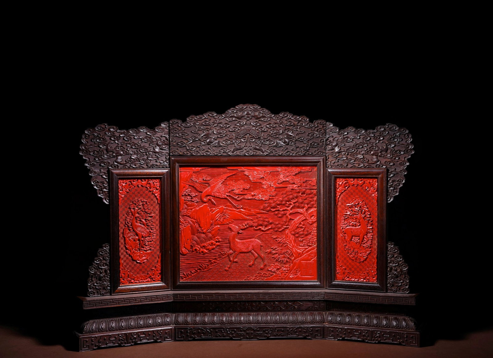 A CARVED CINNABAR LACQUER 'DEER AND CRANE' THREE-FOLD TABLE SCREEN: A CARVED CINNABAR LACQUER 'DEER AND CRANE' THREE-FOLD TABLE SCREEN Dimensions: Length: 58.7 cm (23.11 in.), Height: 39 cm (15.35 in.). All measurements are approximate.