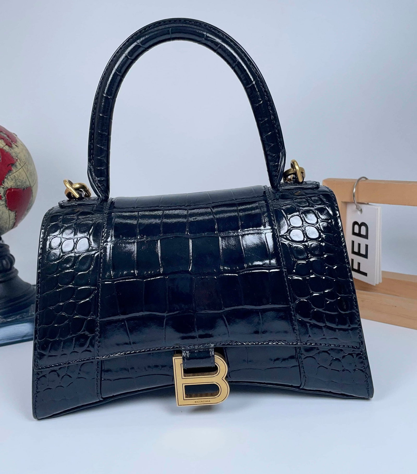 BALENCIAGA HOURGLASS SMALL HANDBAG: BALENCIAGA HOURGLASS SMALL HANDBAG BALENCIAGA, Hourglass, Small. A black crocodile-embossed leather handbag with a sculpted Hourglass silhouette and gold-tone B clasp. Designed for top-handle or