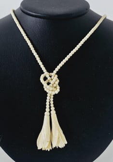 Vintage Carved Bone Tassel Necklace Measures: Measures 34" This is a vintage bone necklace with small, carved beads and two tassel pendants featuring carved flower designs. The necklace is a single open strand, knotted near the bottom to create t