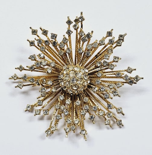 Vintage Gold Tone Rhinestone Starburst Brooch: Unsigned This is a vintage gold-tone starburst brooch adorned with sparkling clear rhinestones. It features a central cluster of round rhinestones, from which numerous rays of textured gold-tone metal