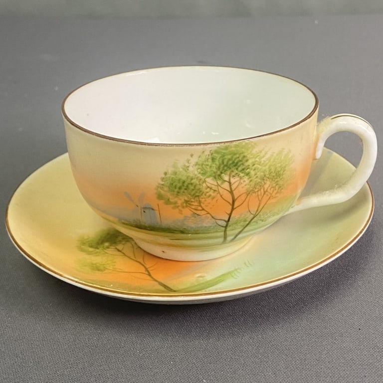 Hand Painted Nippon Teacup and Saucer Hand painted scene of a tree with an orange sky and blue: Hand painted scene of a tree with an orange sky and blue mountains and a windmill in the background. Teacup marked Hand Painted Nippon. No chips, cracks, or crazing. Some discoloration on the bottom o