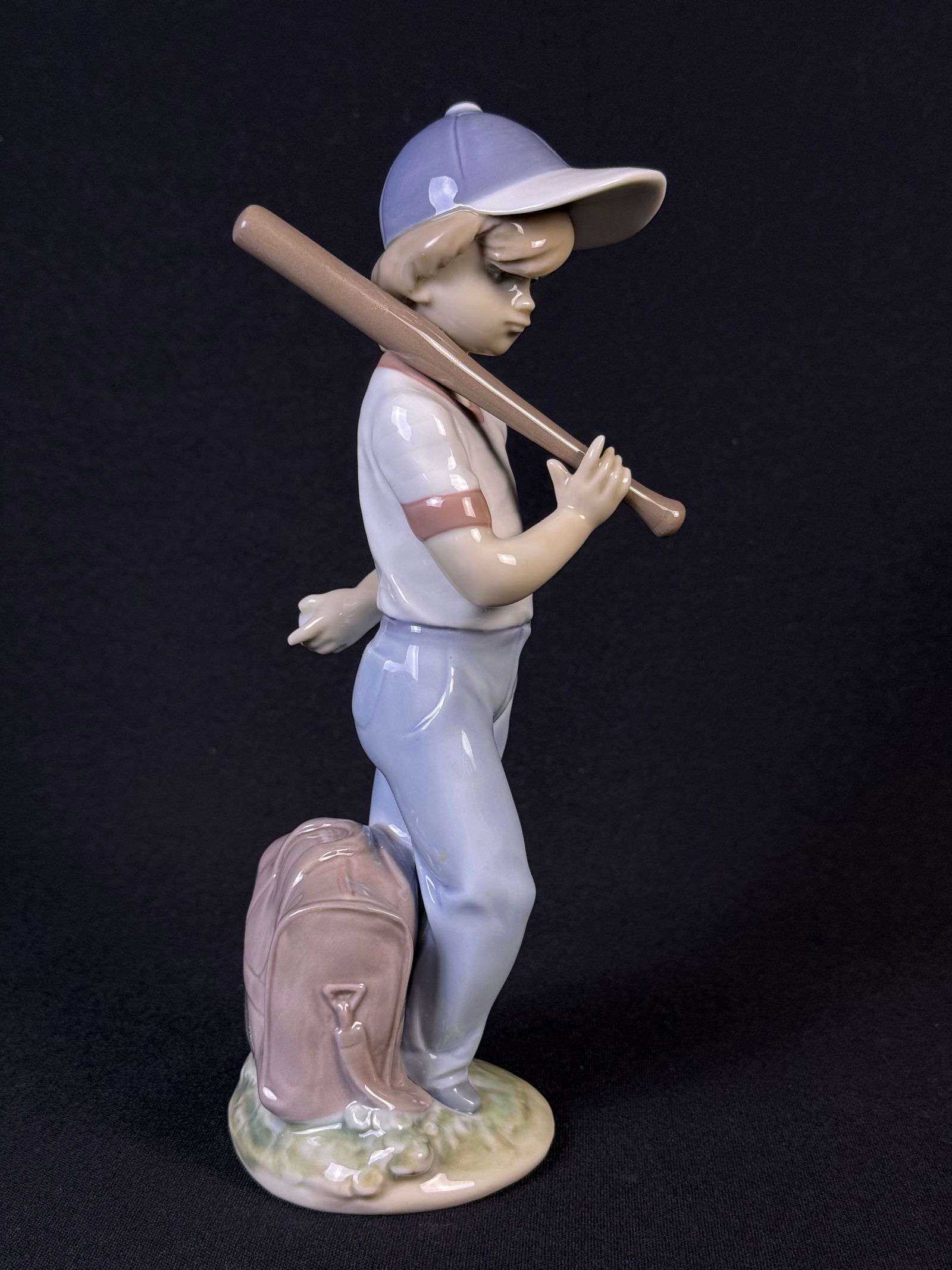 Lladro 'Can I Play' Porcelain Figurine, Model 7610: A Lladro 'Can I Play' porcelain figurine, model 7610. This glazed porcelain figurine depicts a young boy in a light blue baseball cap and uniform, holding a brown baseball bat over his shoulder. A lig