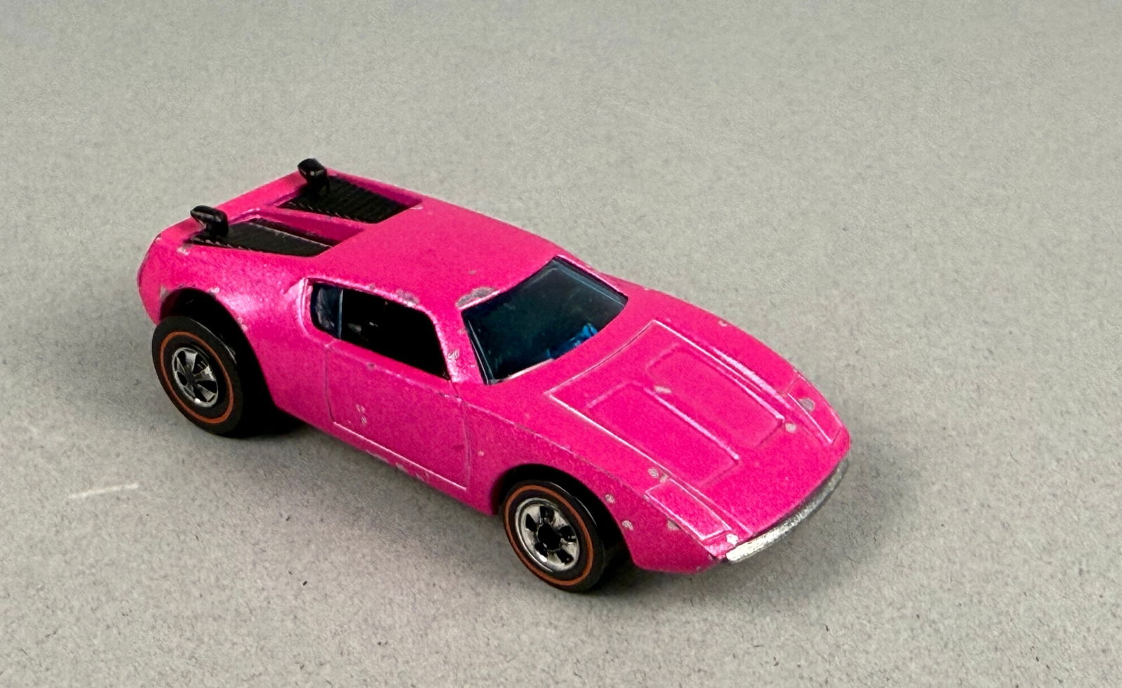 Hot Wheels Redline 1973 Xploder Diecast Car Hot Pink: A vintage Mattel Hot Wheels 1973 Redline Xploder diecast toy car. The vehicle features a rare color metallic pink body with clear blue plastic windows and black plastic interior and engine details, mo