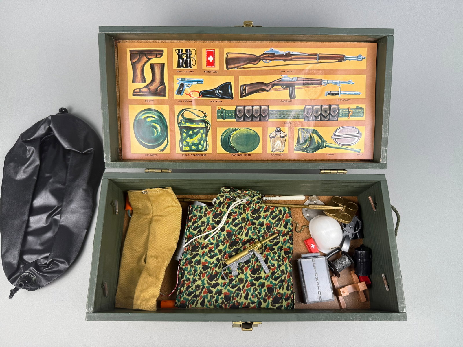 Vintage G.I. Joe Wooden Footlocker with Accessories: A Vintage G.I. Joe Wooden Footlocker with Accessories. The item comprises a dark green painted wooden box with brass-toned hardware. The lid features a "G.I. JOE" decal and stenciled fields for "NAME"