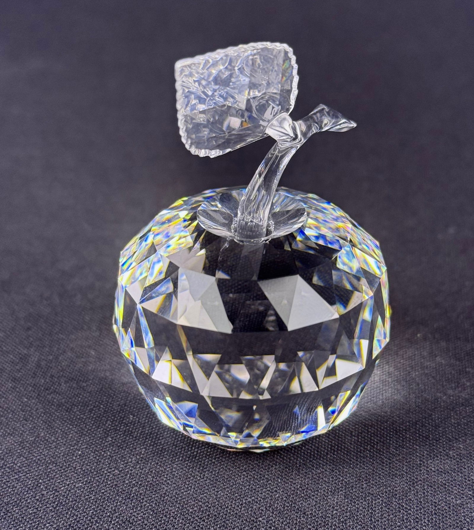 Swarovski Crystal Apple Figurine: A Swarovski crystal apple figurine, crafted from clear, highly faceted crystal or high-quality glass. The extensive faceting on the apple's body creates strong light refraction and dispersion. The pie