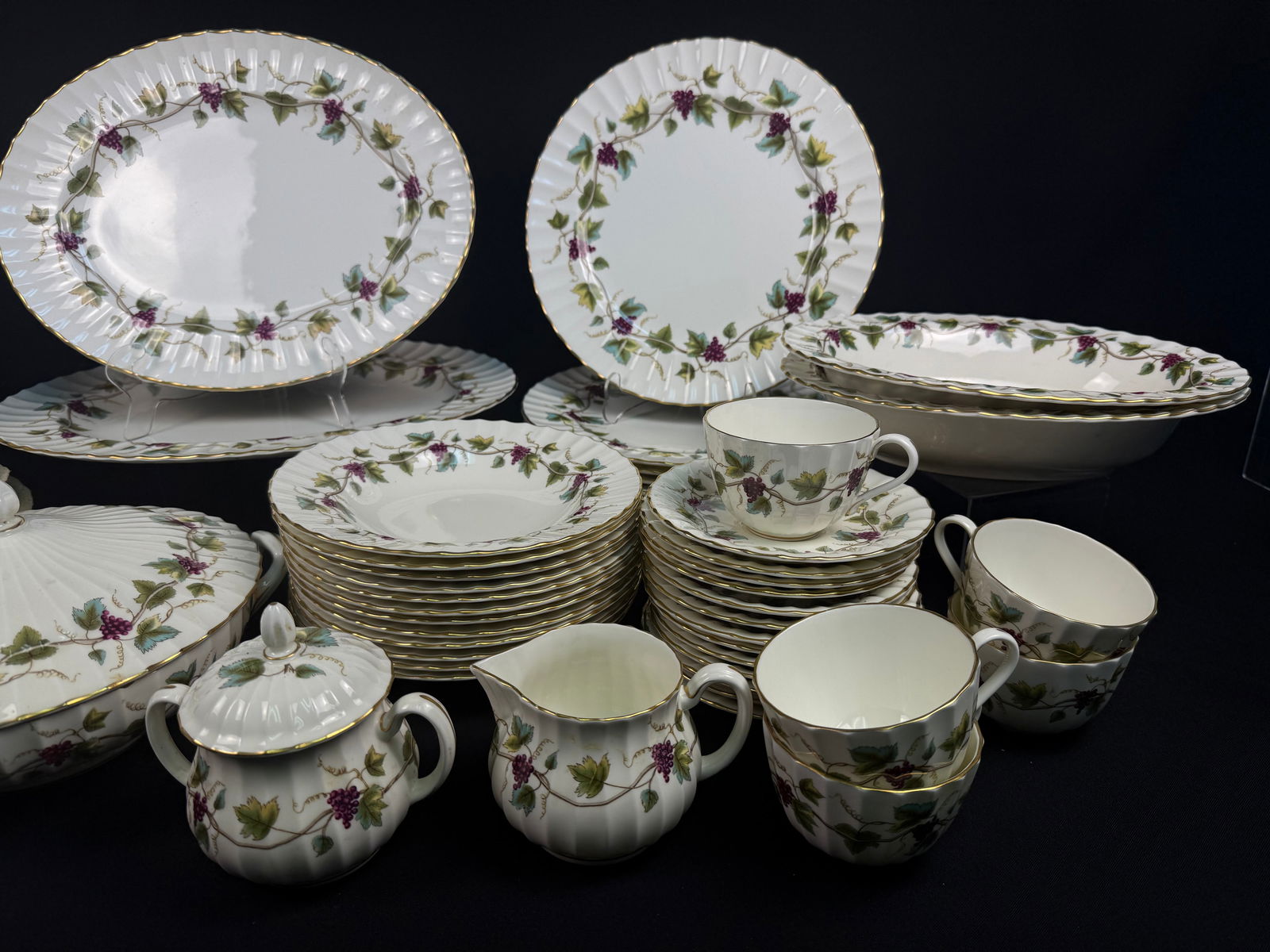 A Royal Worcester 'Bacchanal' Fine Bone China Dinner Service: A Royal Worcester 'Bacchanal' dinner service, crafted from fine bone china, featuring a traditional style with a white ground, scalloped and fluted edges, and elegant gold trim. The decorative pattern