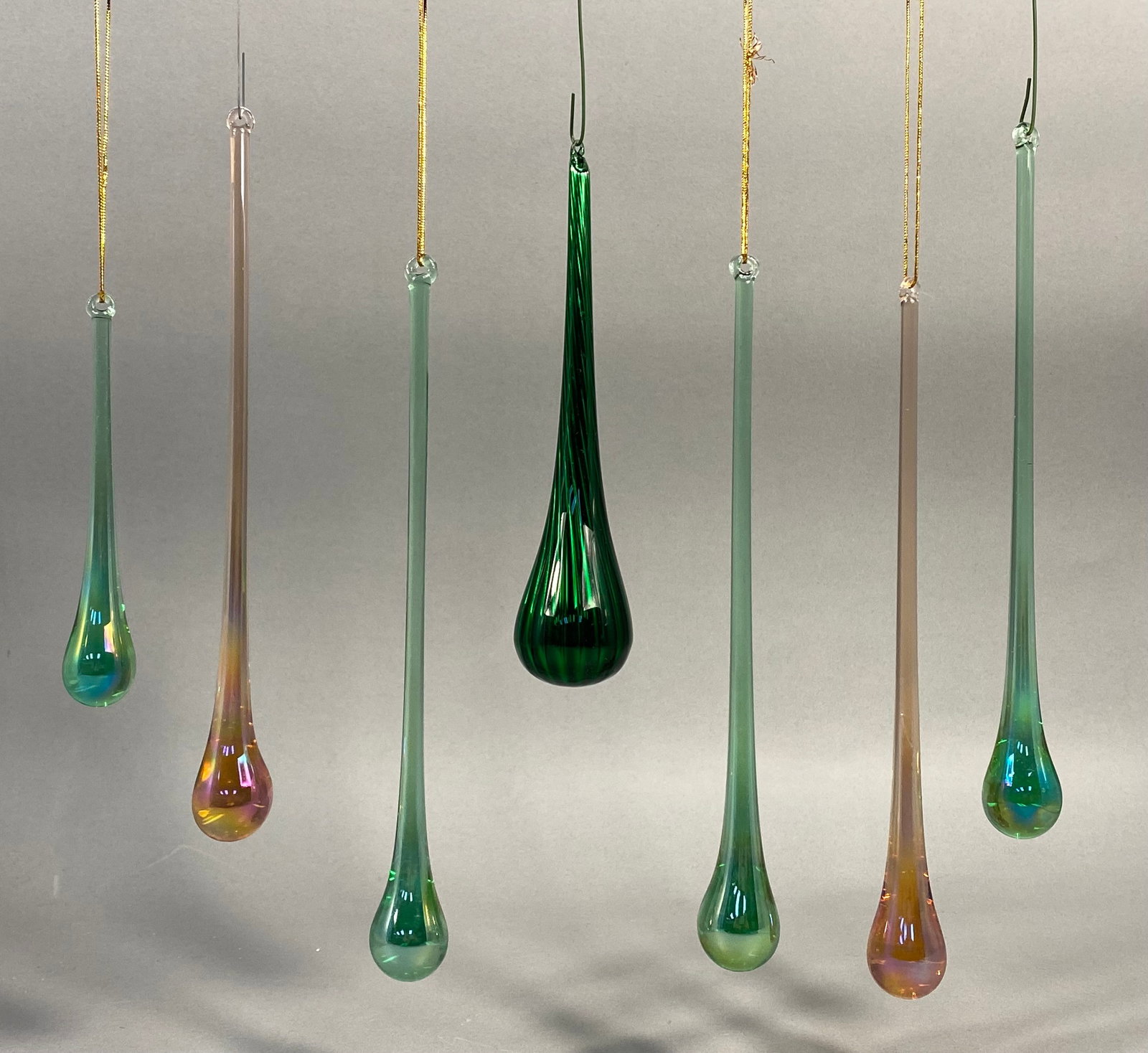 A Set of Seven Sullivans Iridescent Teardrop Glass Ornaments: A set of seven Sullivans iridescent teardrop glass ornaments, serving as ornaments or suncatchers. Six pieces are long and slender, crafted from translucent pale green or champagne-toned glass with ir