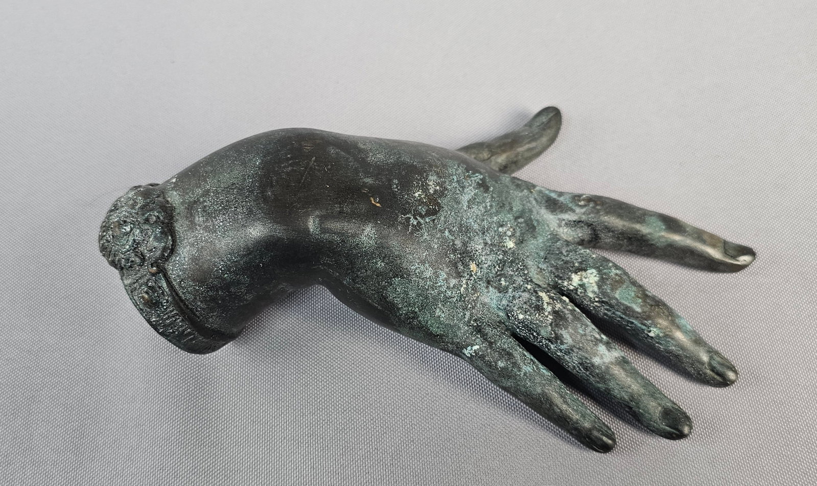 Antique Bronze Hand Sculpture: A bronze hand sculpture, depicting an elongated human right hand with fingers extended and a truncated wrist. The surface features areas of smooth dark patina interspersed with rough, crusty green acc