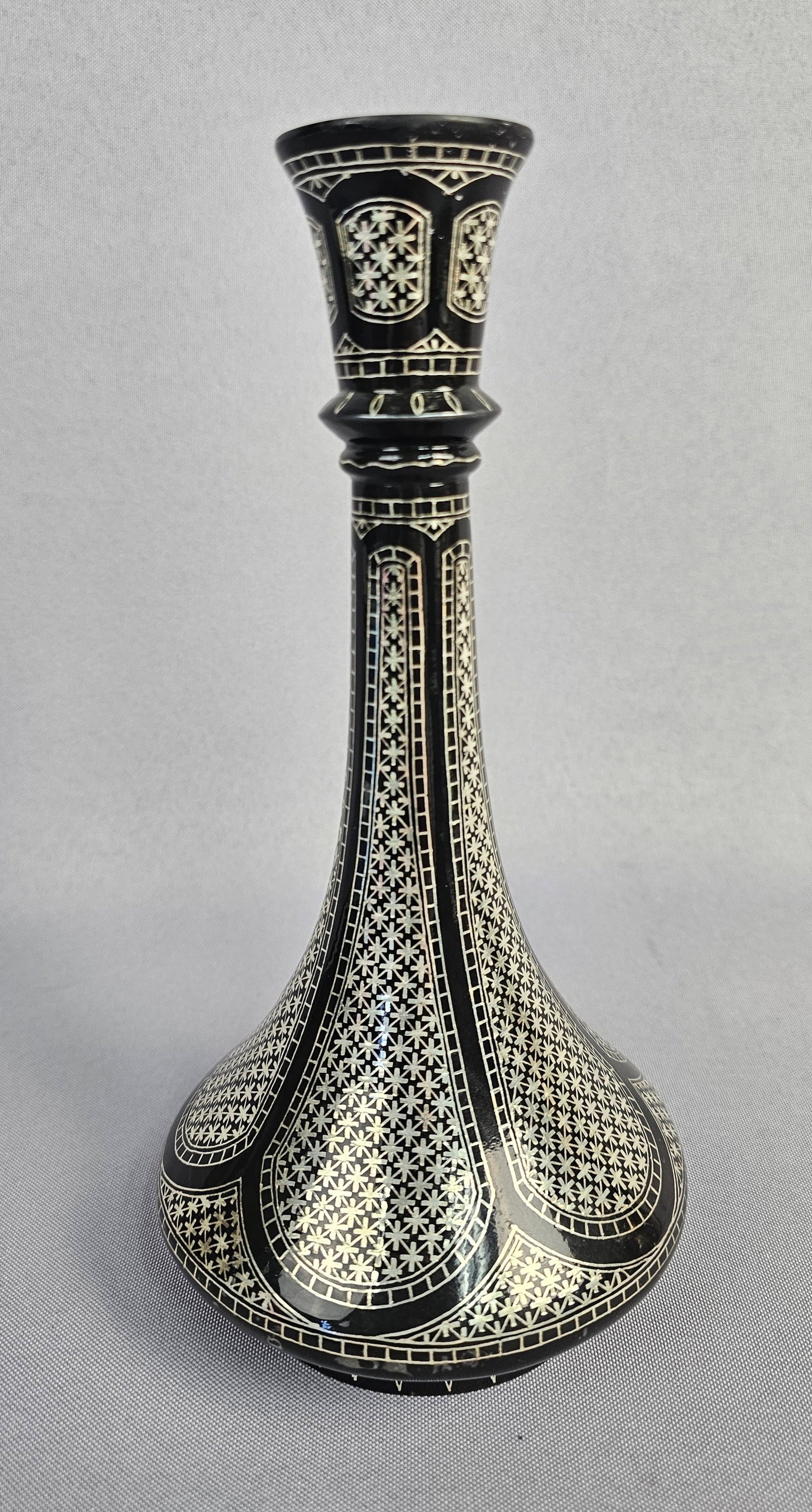A Bidri Ware Vase: A Bidri Ware vase, featuring a flared rim, a slender neck, and a wide, rounded base. The object is extensively embellished with intricate geometric patterns, including tessellating star motifs, formed