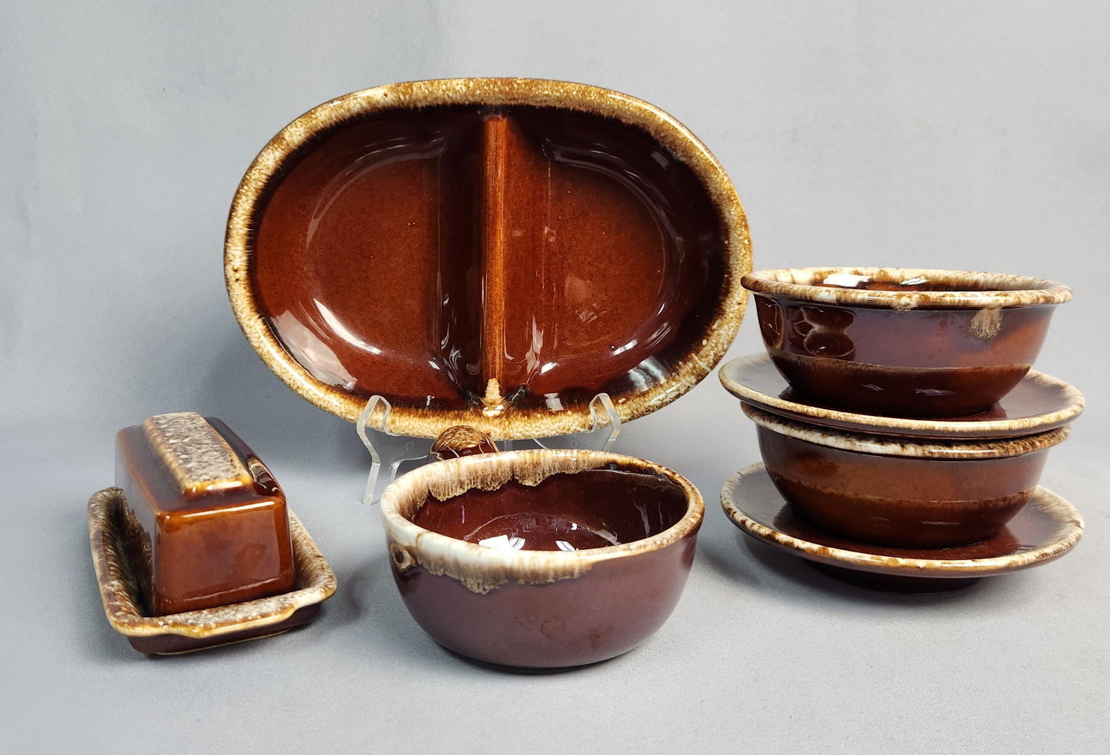 A Collection of Hull 'Brown Drip' and 'Crestone' Dinnerware with a McCoy Handled Bowl: A collection of glazed ceramic dinnerware and serveware, primarily by Hull Pottery in their 'Brown Drip' style, accompanied by a single handled bowl by McCoy. The Hull pieces feature a deep, glossy br