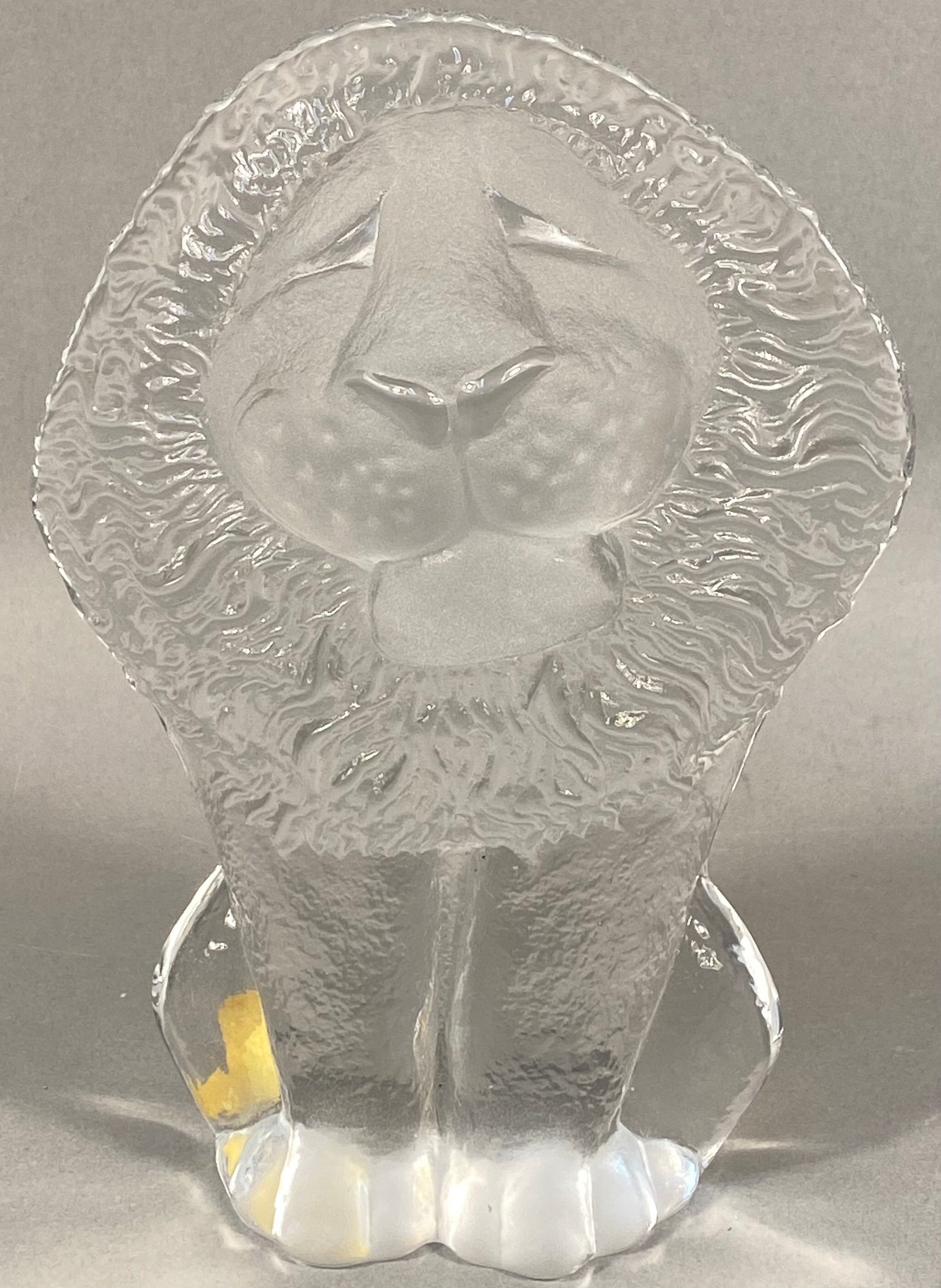 Mats Jonasson Royal Krona Crystal Lion Paperweight: A Mats Jonasson Royal Krona crystal lion paperweight. This clear molded glass figurine depicts a stylized lion with a textured mane and frosted details on its face, including closed eyes, a prominent