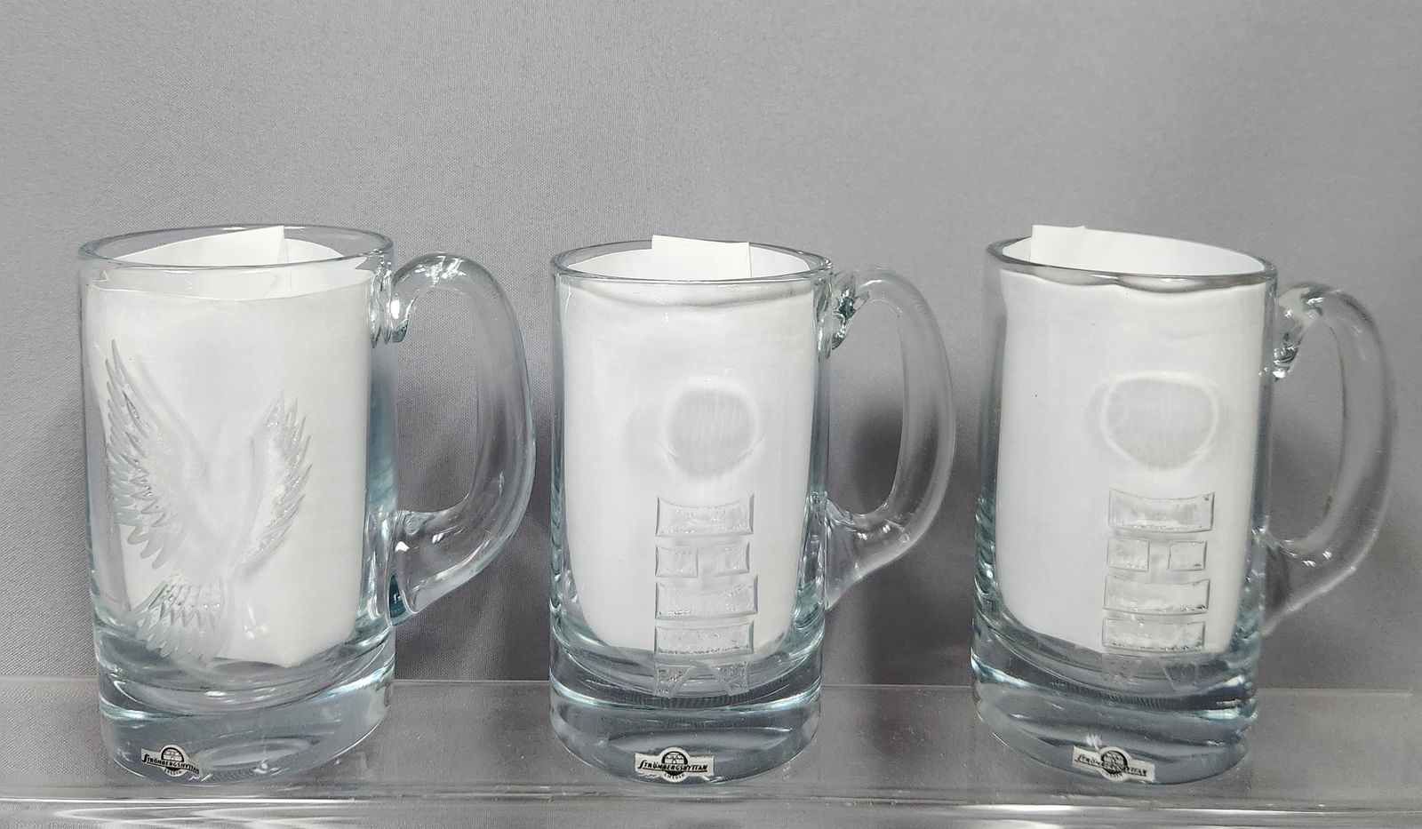 Three Strombergshyttan Limited Edition Crystal Tankards by E. A. Garand and Paul Rene Gauguin, Early: A group of three clear crystal glass tankards by Strömbergshyttan, Sweden, dating to the early 1970s. One tankard, from 1971, features an etched motif of a peaceful dove and is identified by a pa