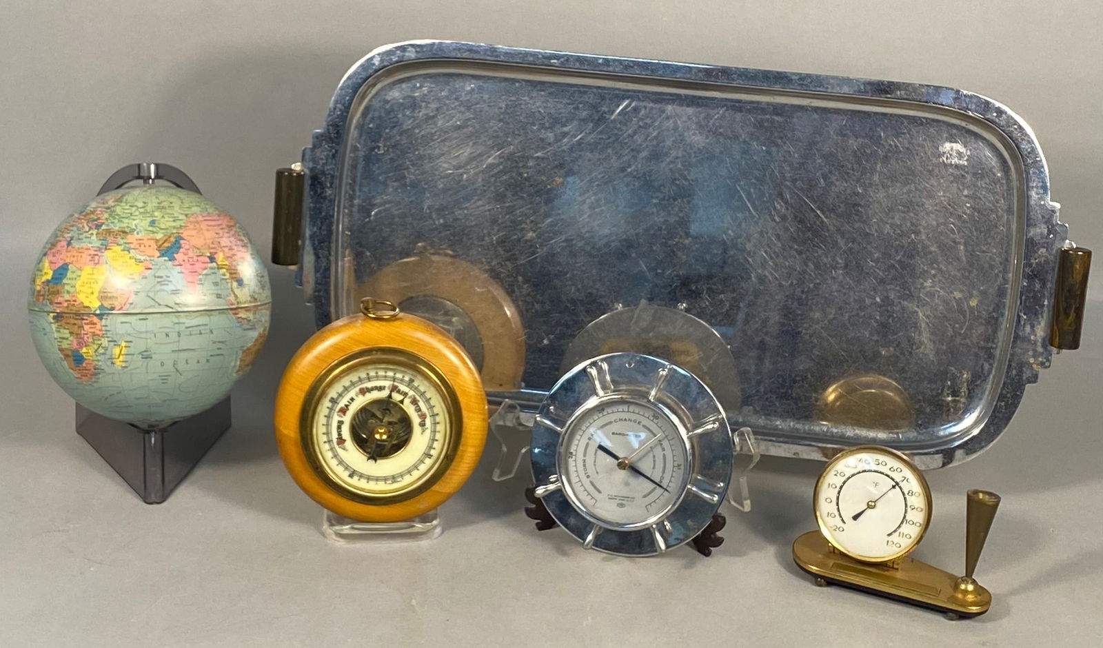 A Collection of Vintage Desk Accessories, Barometers, and Tray: This lot features a diverse collection of vintage items. It includes a small, multi-colored desk globe on a dark plastic stand. Also present are two barometers: one circular barometer in a light woode