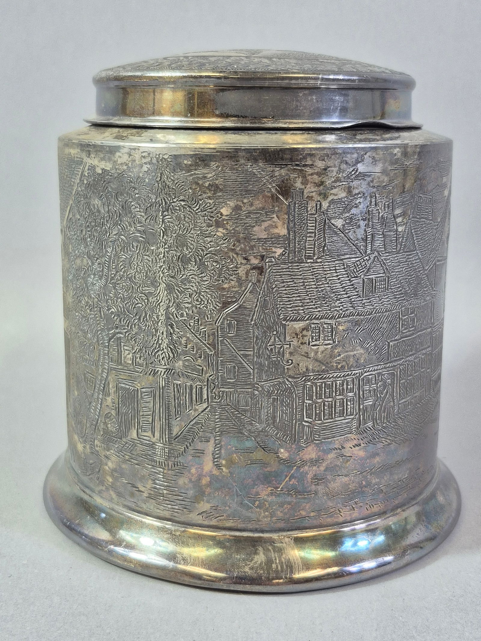 Reed & Barton Silver-Plated 'Blue Boar Inn' Humidor, circa 1890s: A Reed & Barton silver-plated 'Blue Boar Inn' humidor, circa 1890s. This cylindrical, lidded metal container features an extensively engraved continuous panoramic scene depicting a bustling villag