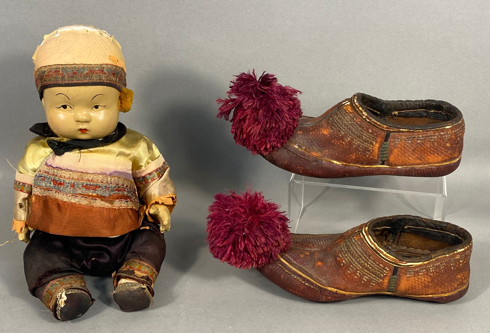 A Ming Ming Chinese Composition Doll and a Pair of Traditional Shoes: A Ming Ming Chinese composition doll featuring a composition head with painted facial features, including almond-shaped eyes and red lips. The doll is dressed in a multi-layered fabric outfit comprisi