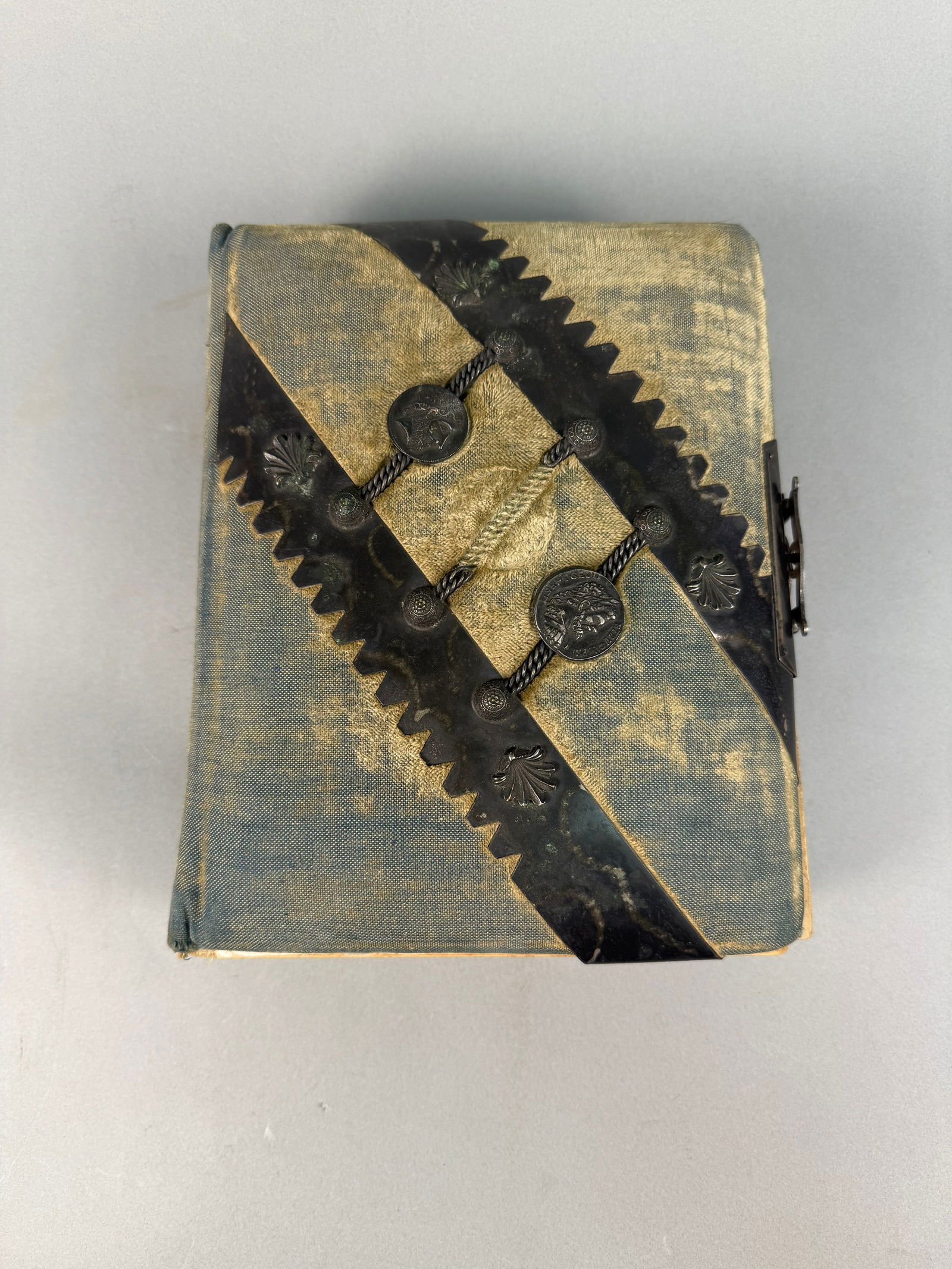 Late 19th to Early 20th Century Antique Fabric and Metal Mounted Photograph Album: An antique photograph album dating from the late 19th to early 20th century. The album features a fabric cover with a faded blue/teal and gold/yellow diagonal pattern. It is embellished with decorativ