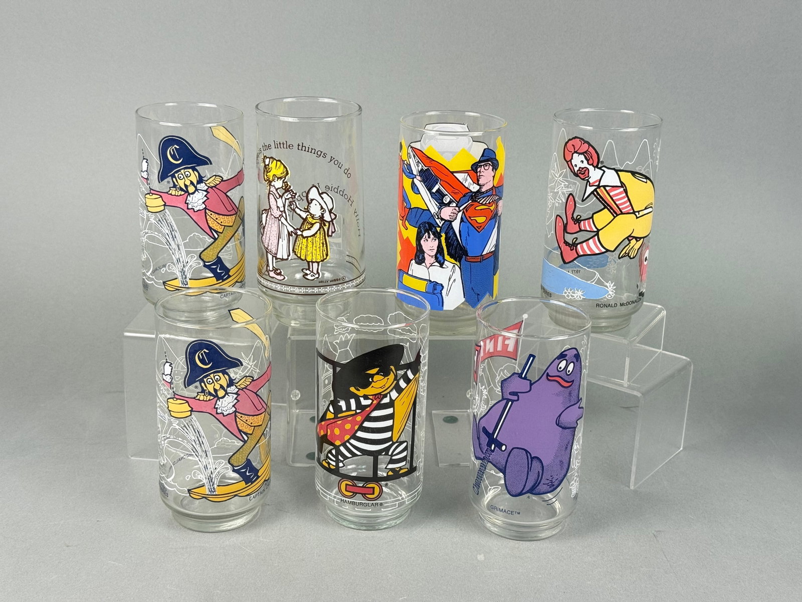 A Collection of 1977 McDonaldland Action Series and Other Advertising Glasses: A collection of eight clear glass tumblers. This lot includes five glasses from the 1977 McDonaldland® Action Series, depicting characters such as Captain Crook (twice), Ronald McDonald, Grimace, 